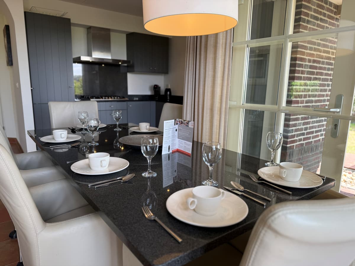 Eetkamer met een moderne tafel gedekt voor vier personen, naast een grote glazen deur met uitzicht naar buiten.