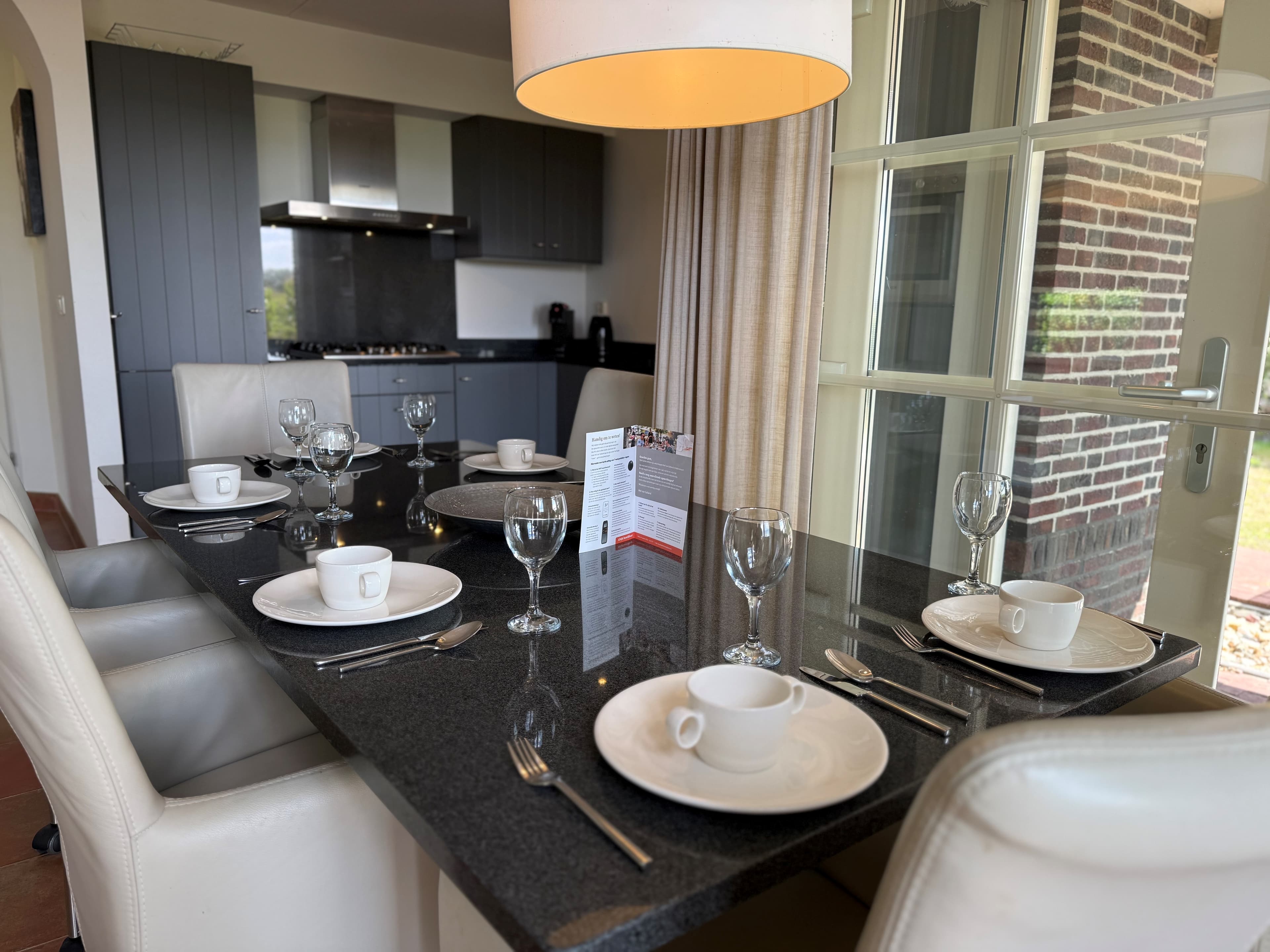 Eetkamer met een moderne tafel gedekt voor vier personen, naast een grote glazen deur met uitzicht naar buiten.