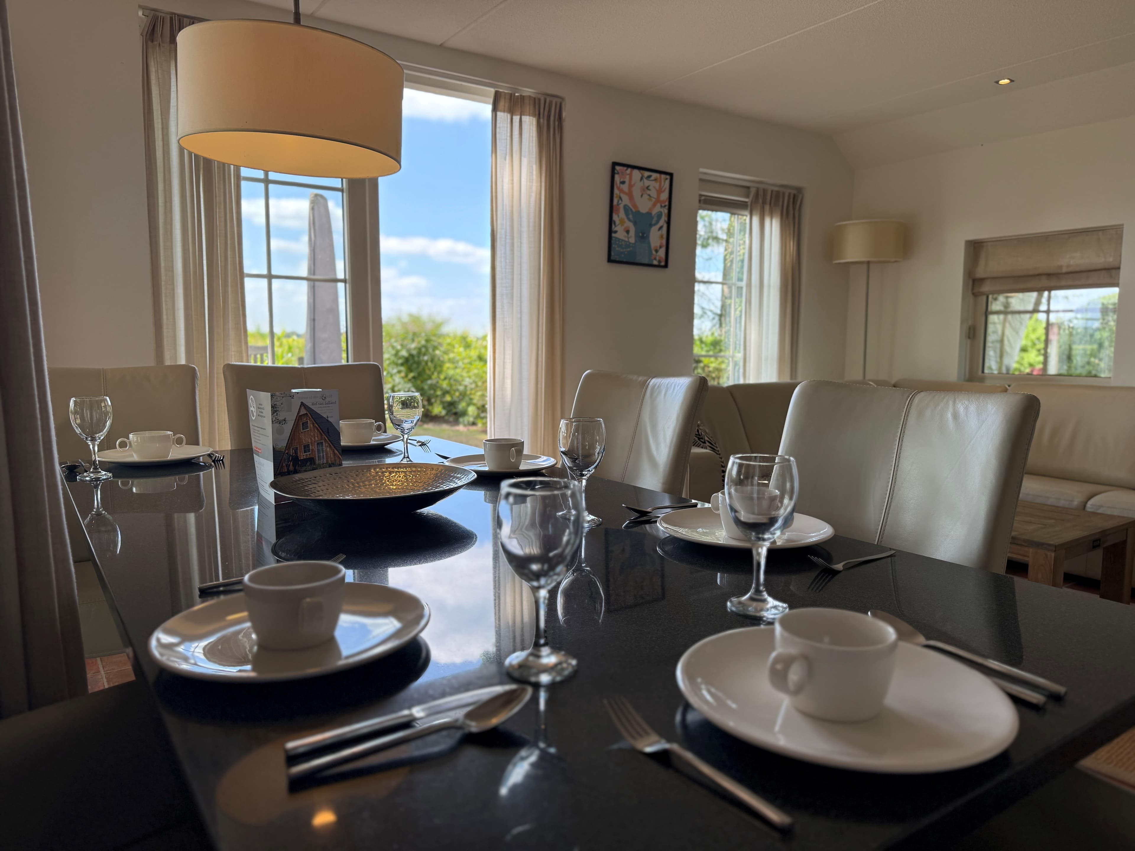 Eettafel met gedekte plaatsen, lichte meubels en grote ramen met uitzicht op groen vanaf de recreatiewoning