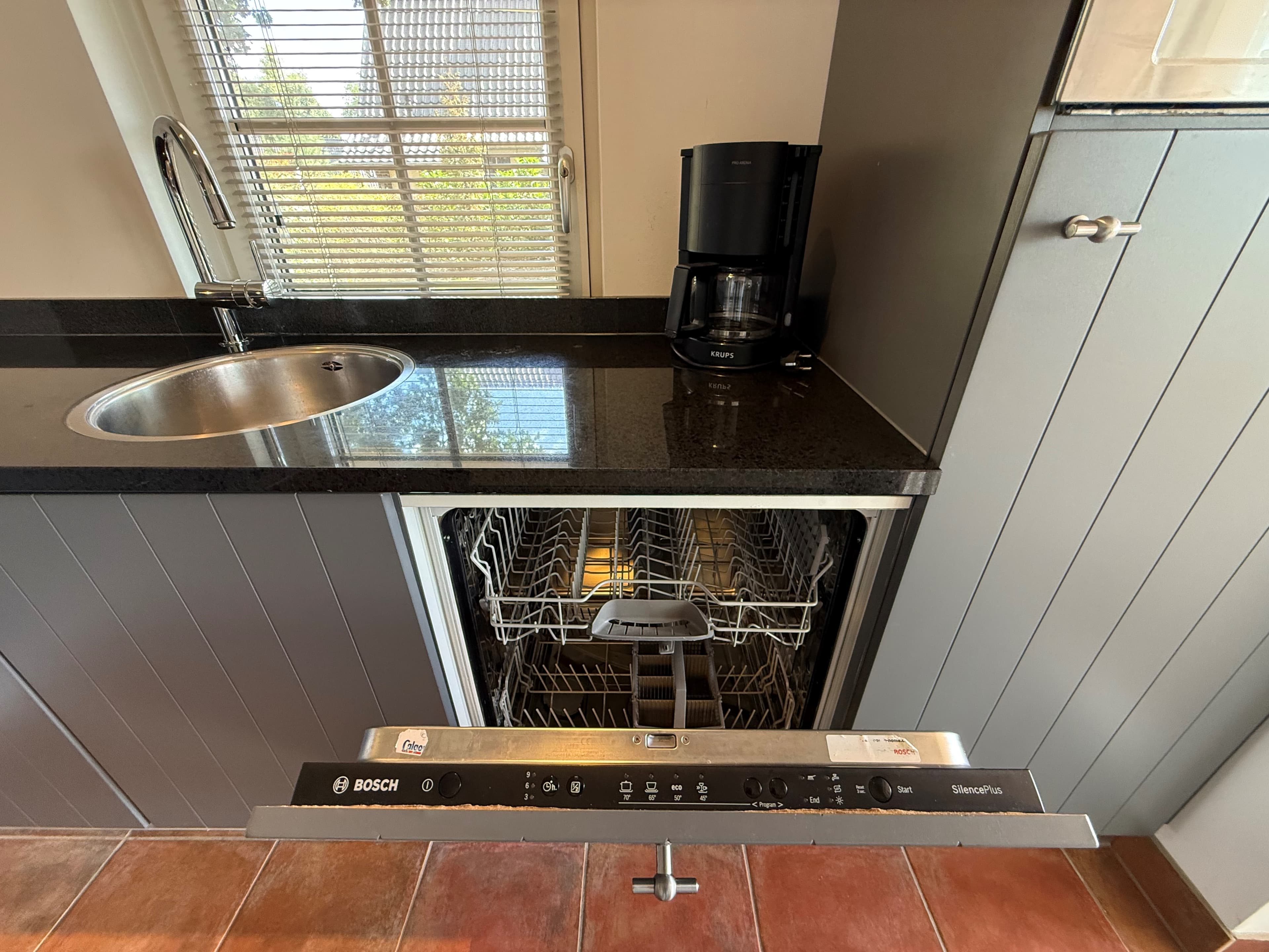 Keuken met een zwart aanrechtblad, spoelbak, vaatwasser en koffiezetapparaat nabij een raam.