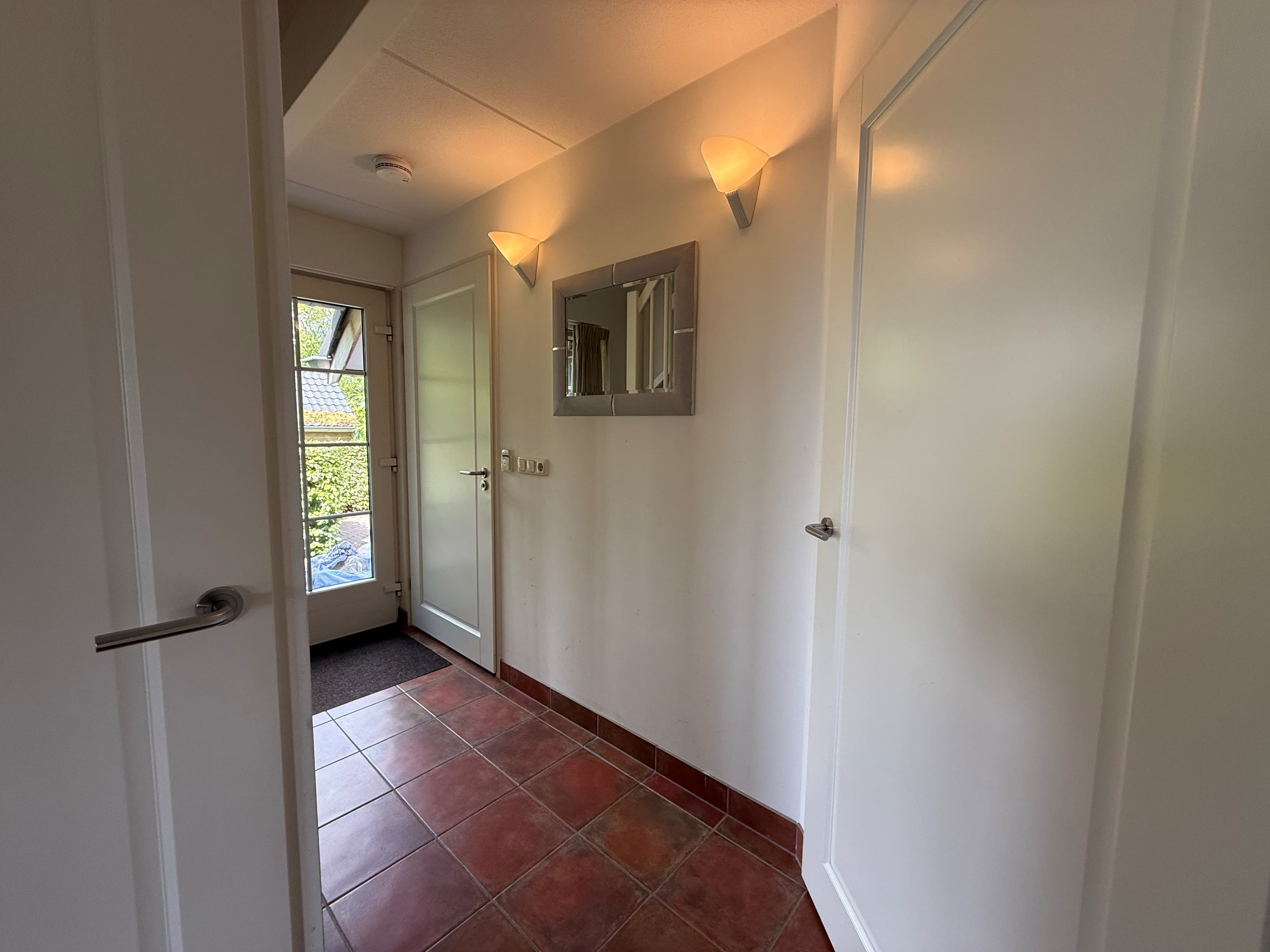 Entree van de recreatiewoning met tegelvloer, wandlampen en deuren naar andere ruimtes.