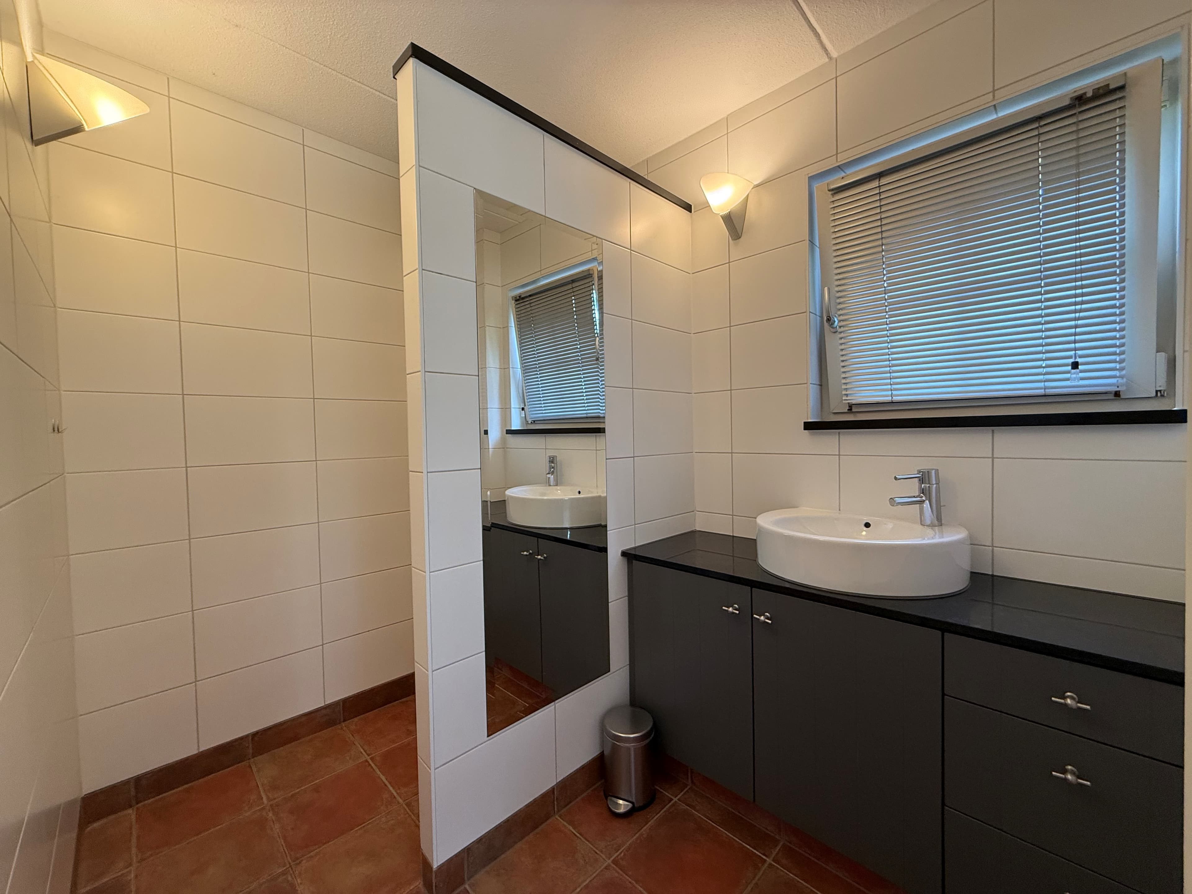 Moderne badkamer met grote spiegel, wastafel en opbergkasten in lichte en donkere kleuren.