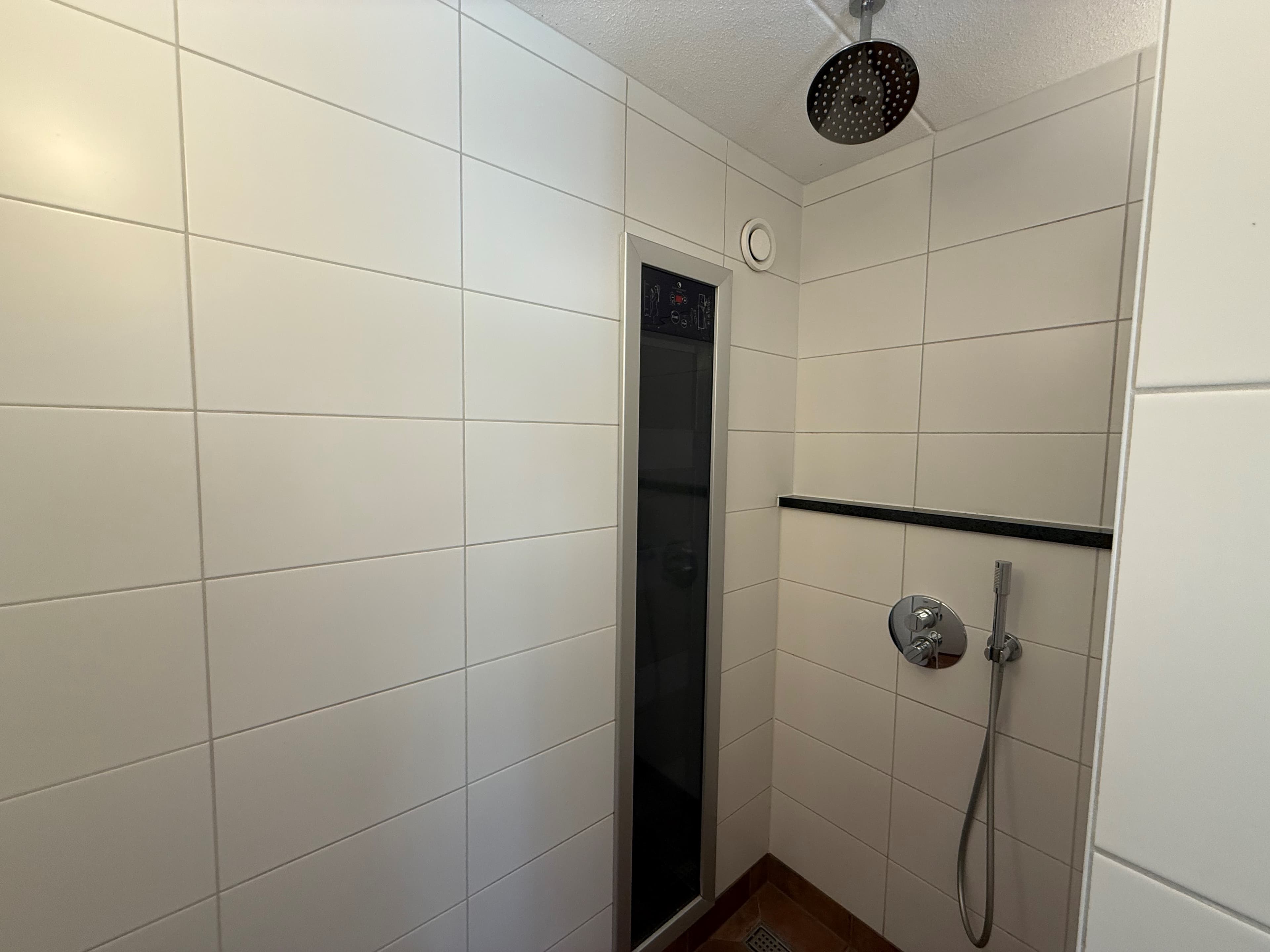 Badkamer met inloopdouche, betegelde wanden en een moderne douchestang met handdouche en regendouchekop.