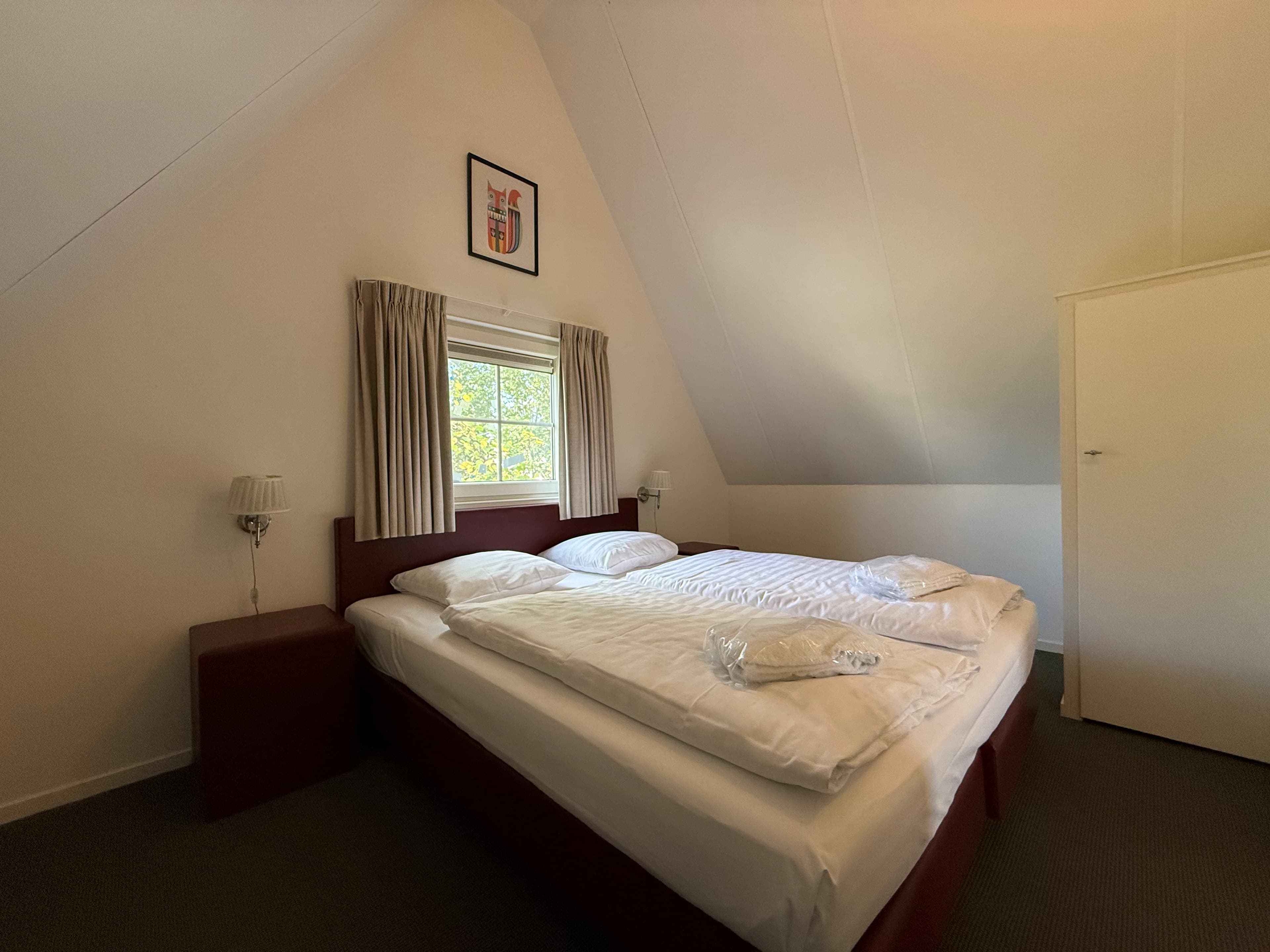 Slaapkamer met een tweepersoonsbed, nachtkastjes en een raampartij met gordijnen.