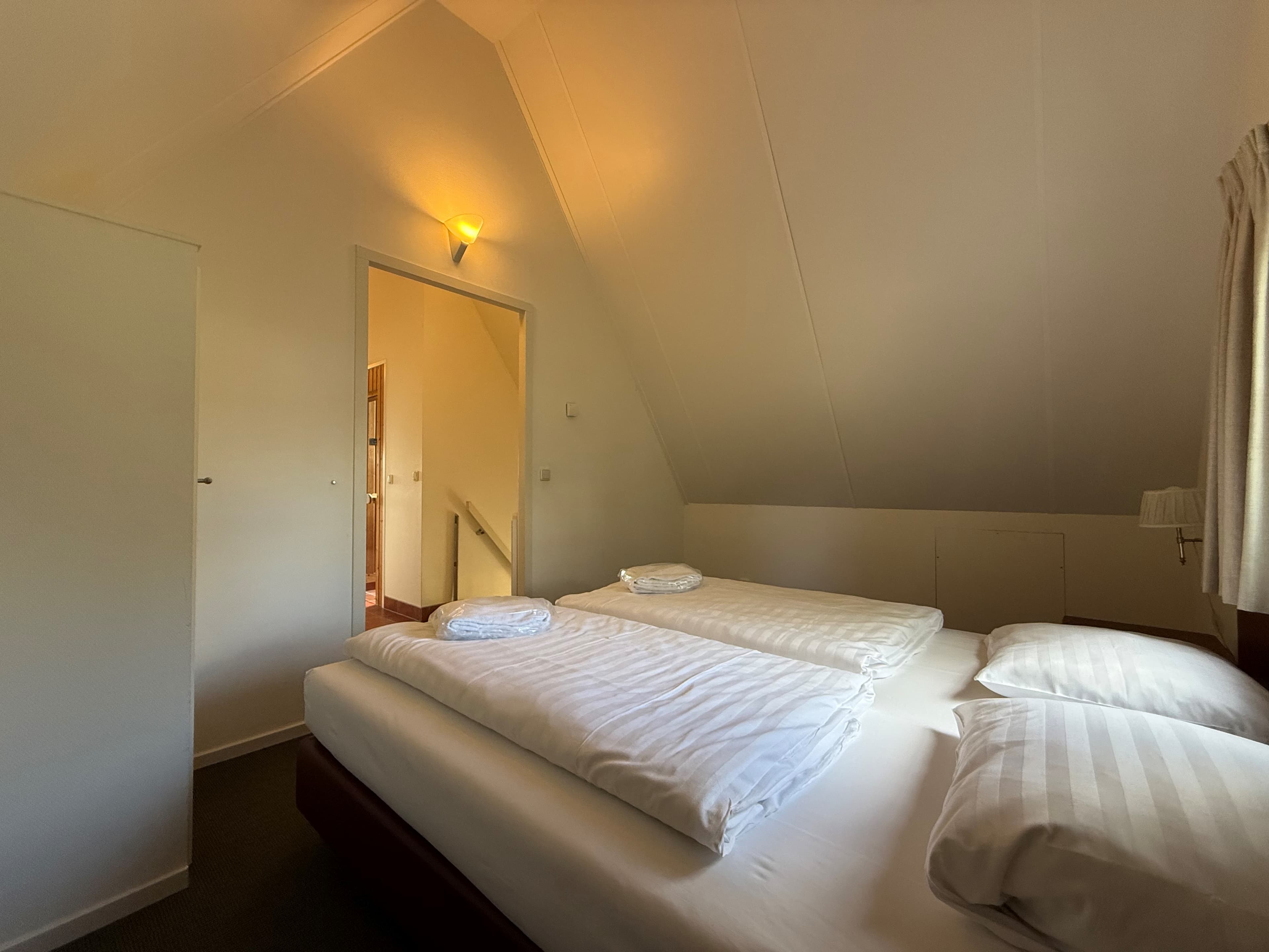 Slaapkamer met twee eenpersoonsbedden, een witte kast en een deur naar een gang met trap.