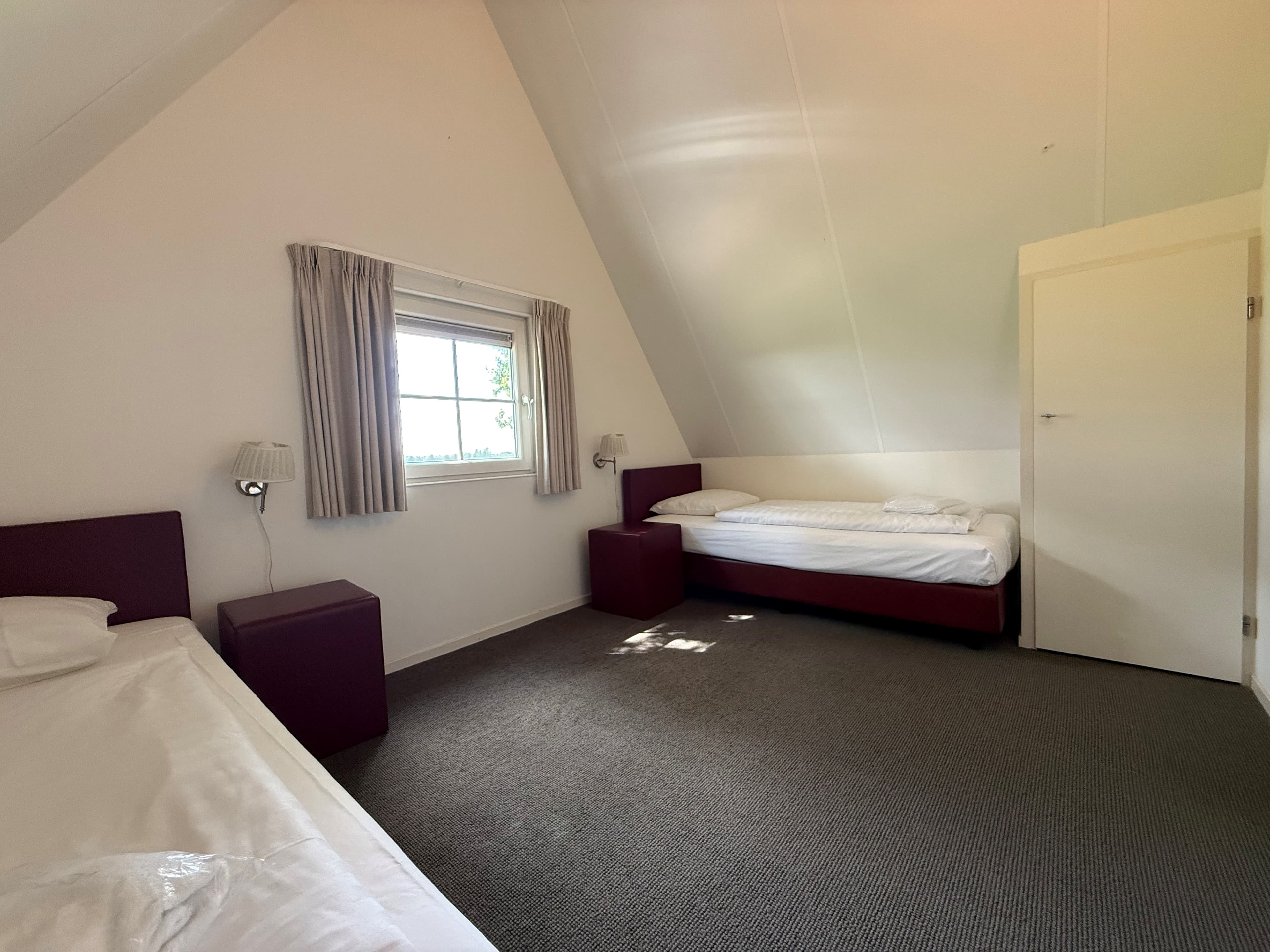 Slaapkamer met twee eenpersoonsbedden, een tweepersoonsbed en een raam met uitzicht naar buiten.
