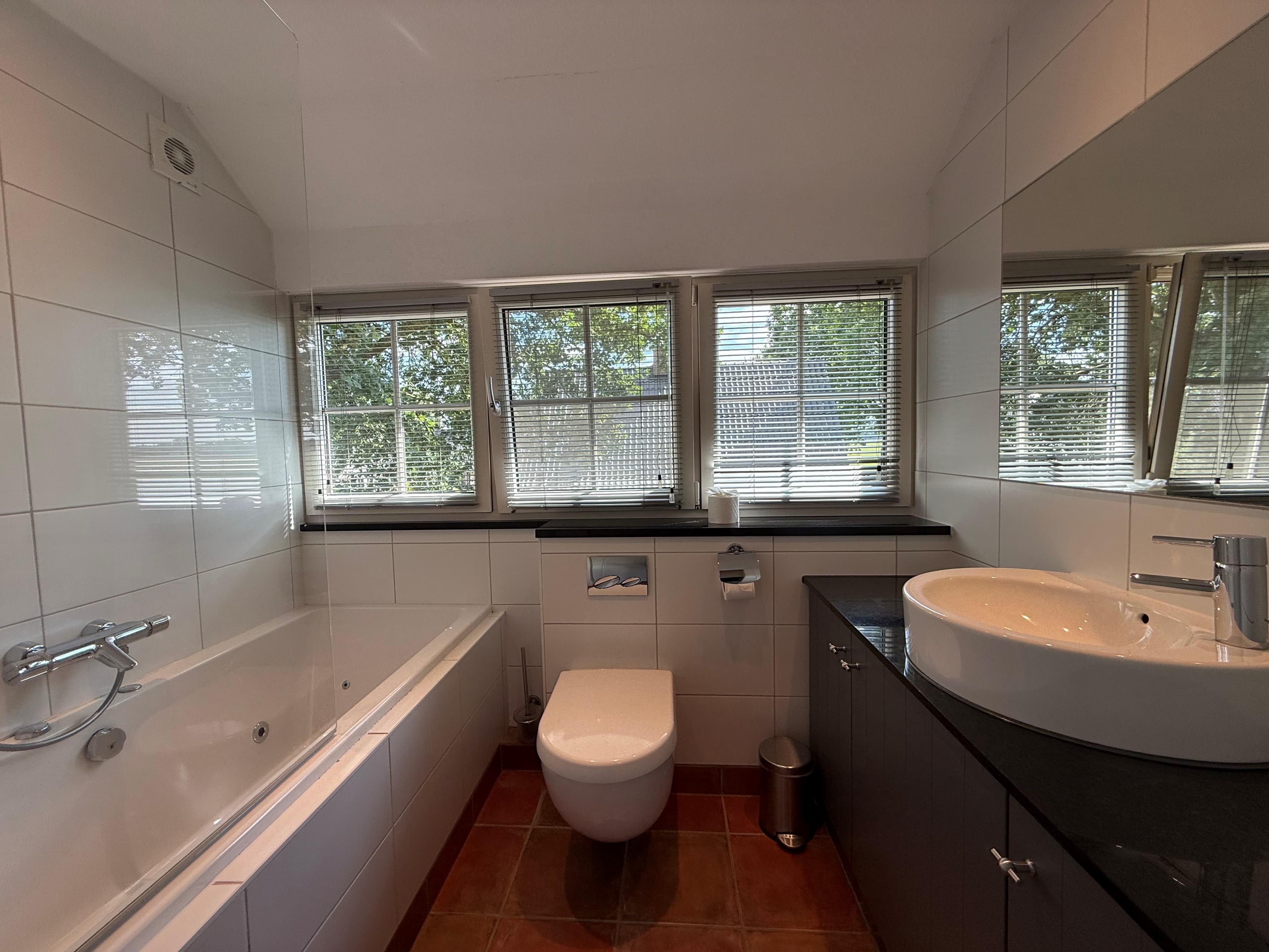 Moderne badkamer met ligbad, toilet, wastafel en grote ramen voor natuurlijk licht