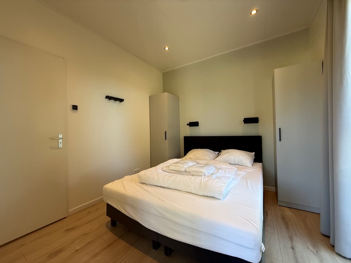 Slaapkamer met een tweepersoonsbed, twee kastjes en hangplaatsen aan de muur, lichte wanden en houten vloer