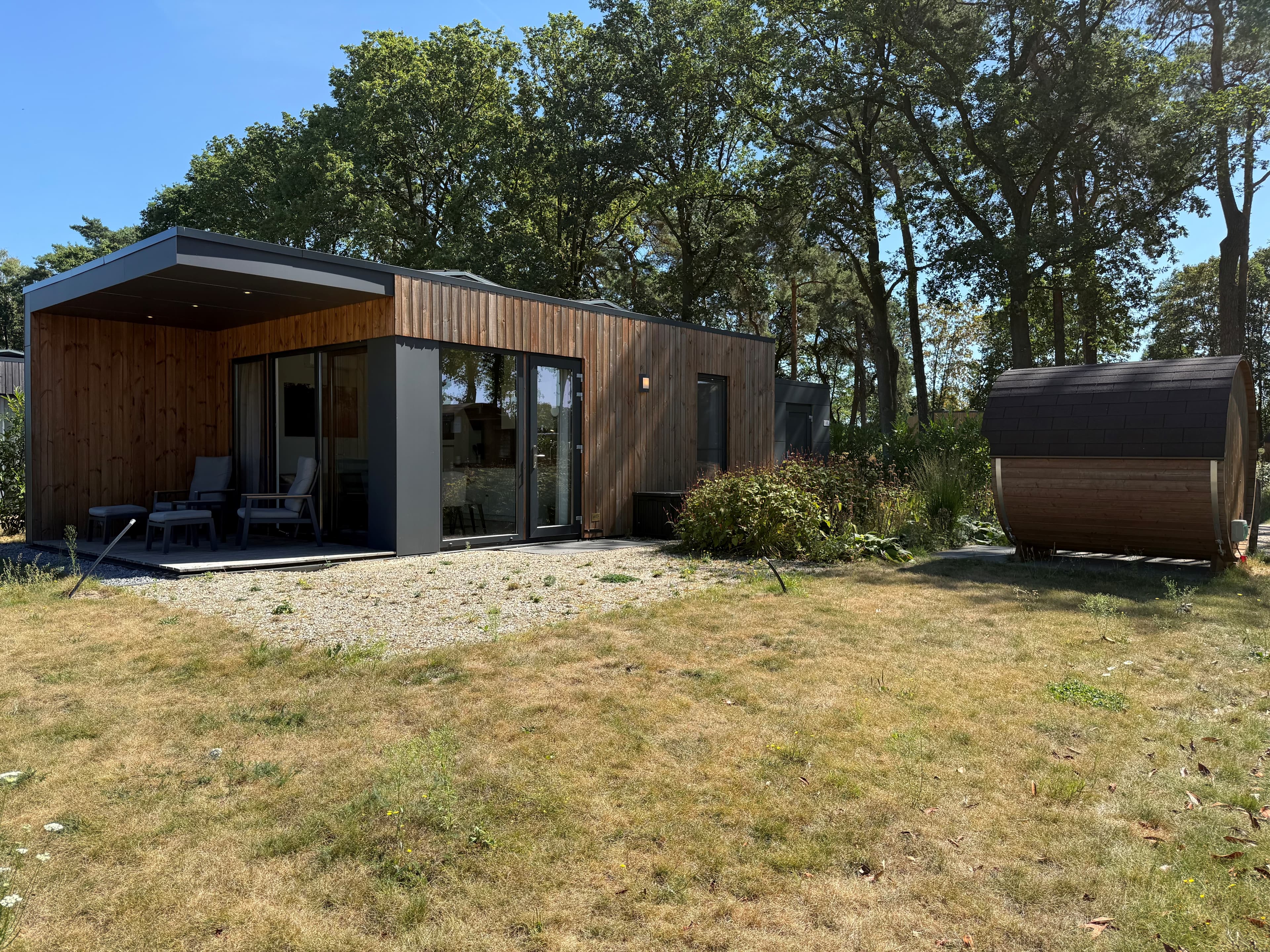 Moderne woning met houten gevel, glazen schuifdeuren, en een tuin met gras en een sauna in het buitengebied