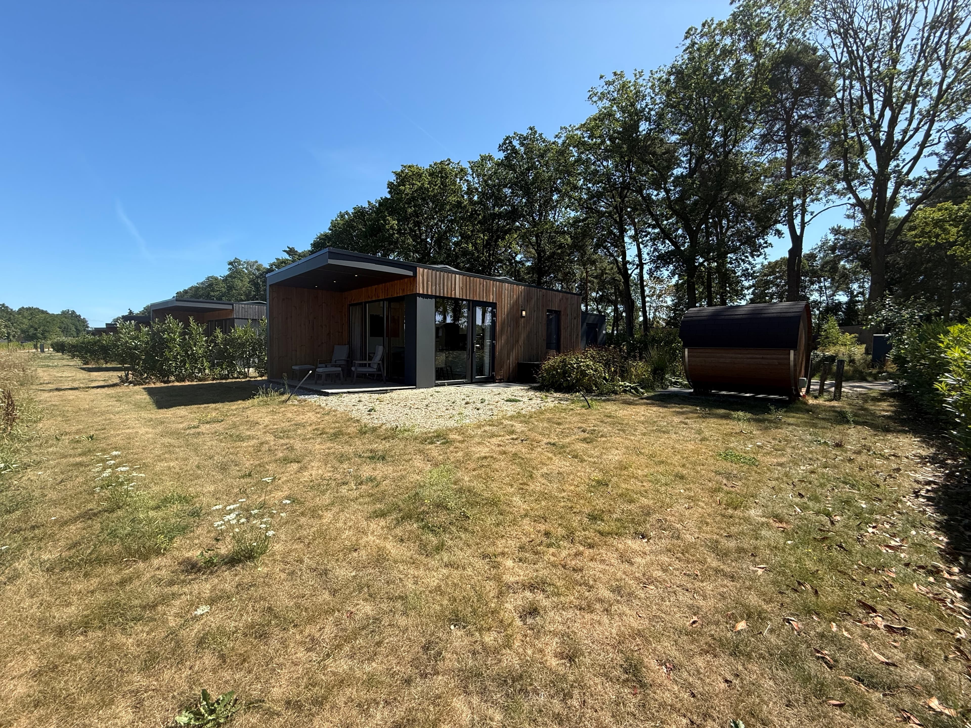 Moderne vakantiewoning met houten gevel, grote ramen en een tuin omringd door bomen en struiken