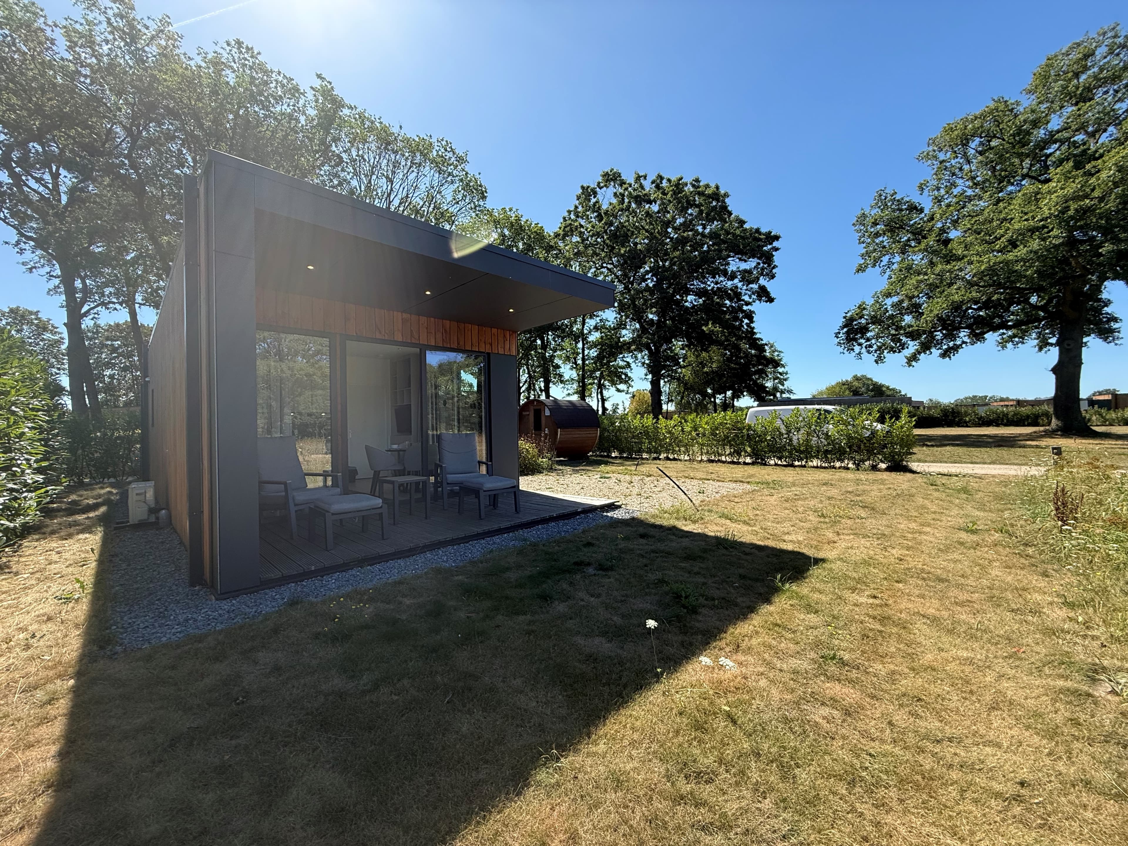 Moderne vakantiewoning met een veranda, omringd door gras en bomen in een groene omgeving