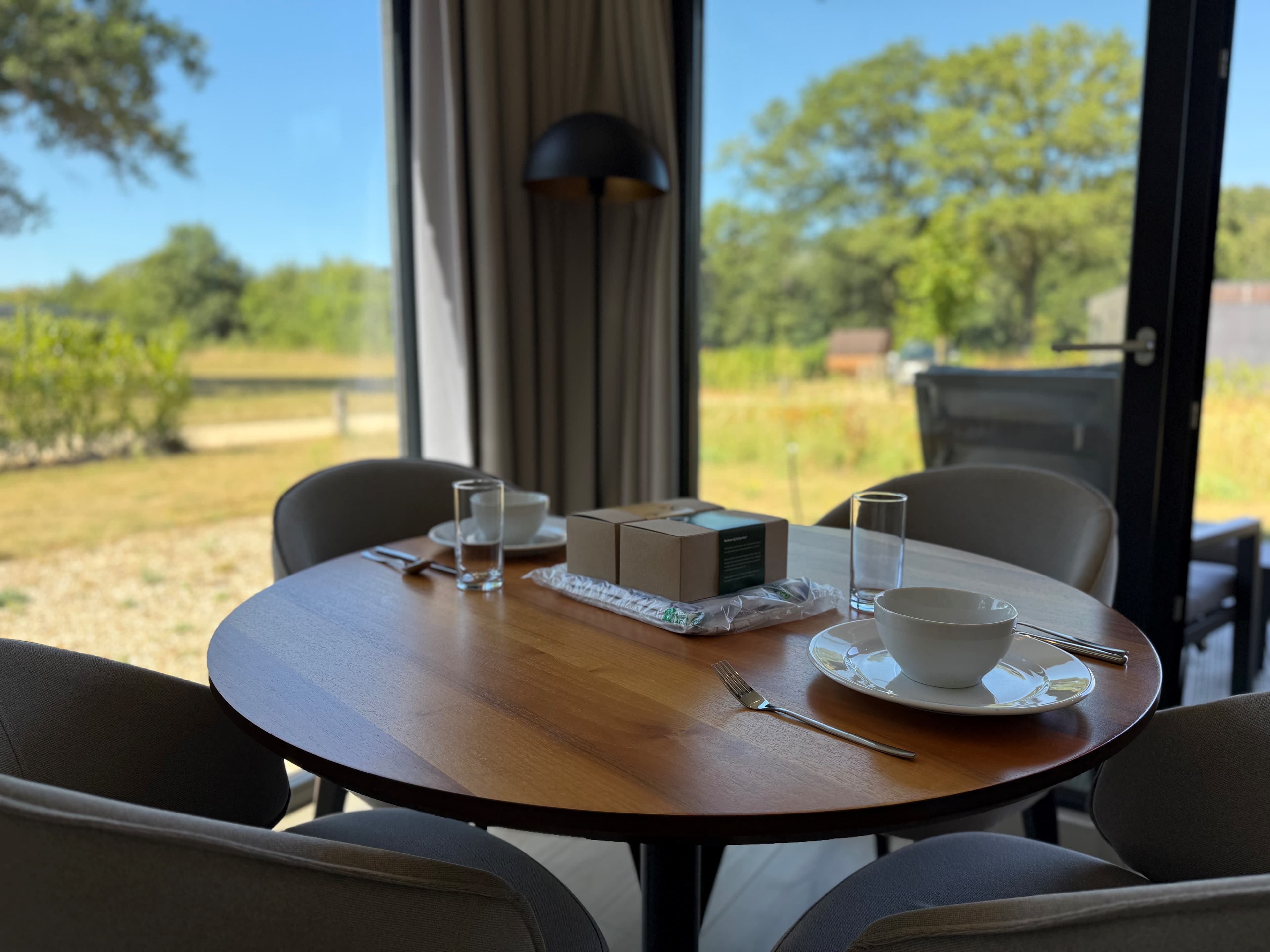 Eettafel met servies en glazen, uitzicht op een groene omgeving door grote raampartij