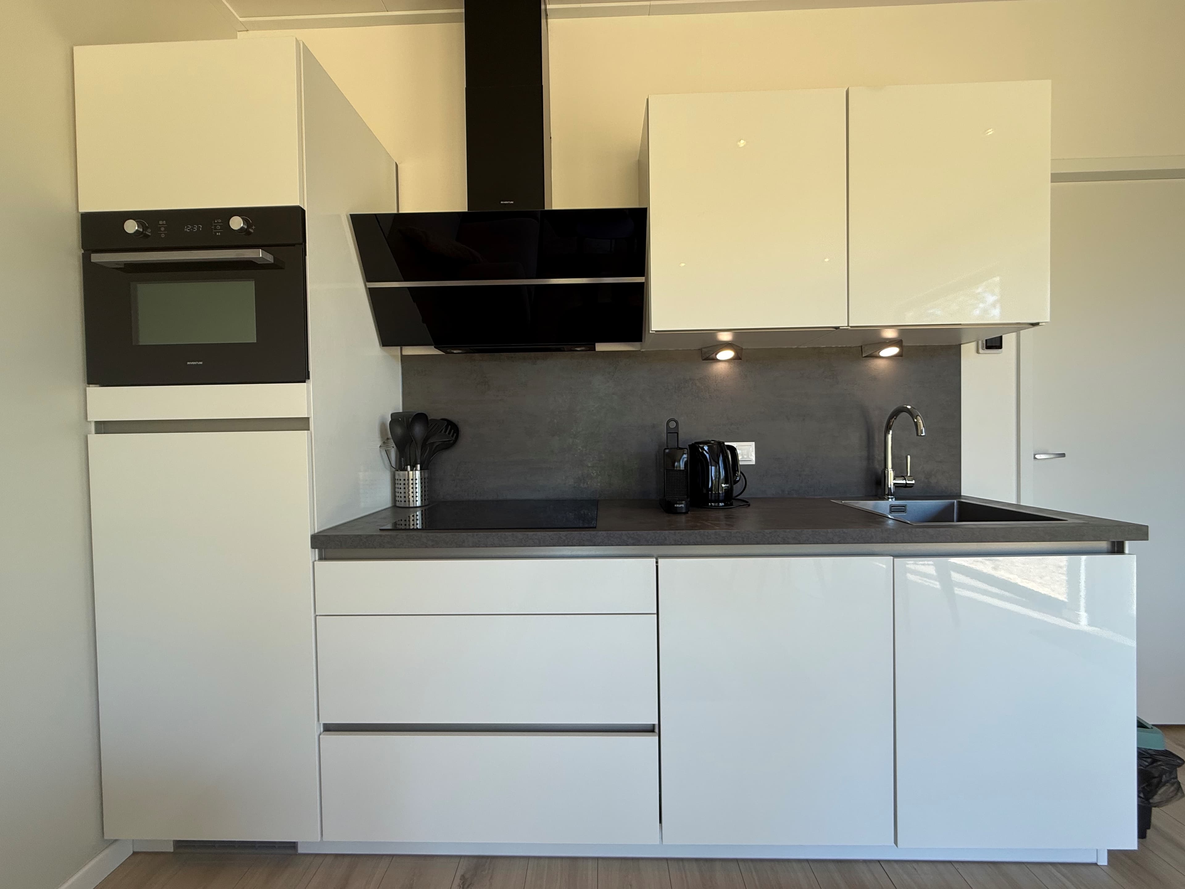 Moderne keuken met witte kasten, zwarte werkblad, oven, inductiekookplaat en apparatuur zoals een waterkoker en een spoelbak