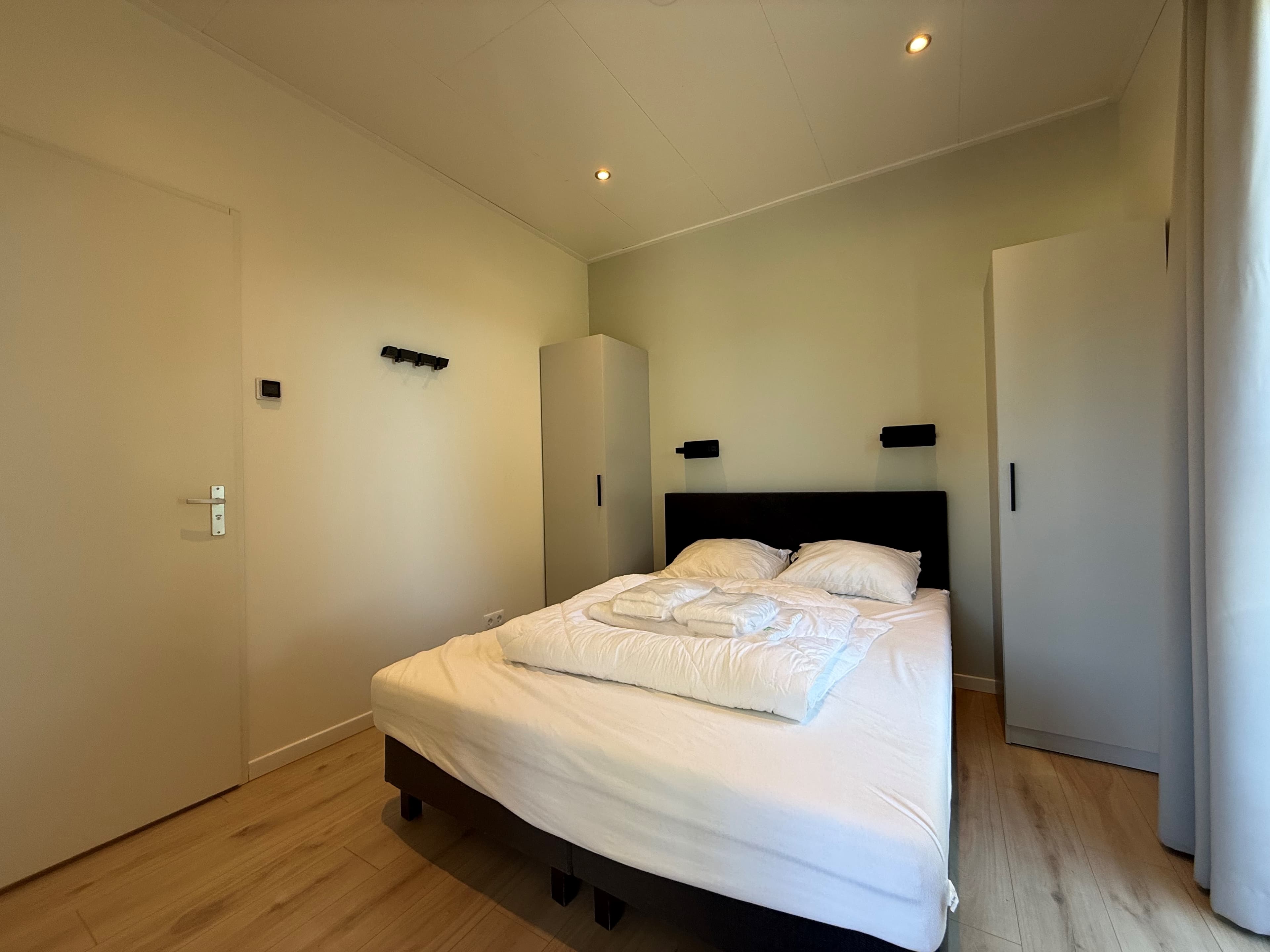 Slaapkamer met een tweepersoonsbed, twee kastjes en hangplaatsen aan de muur, lichte wanden en houten vloer