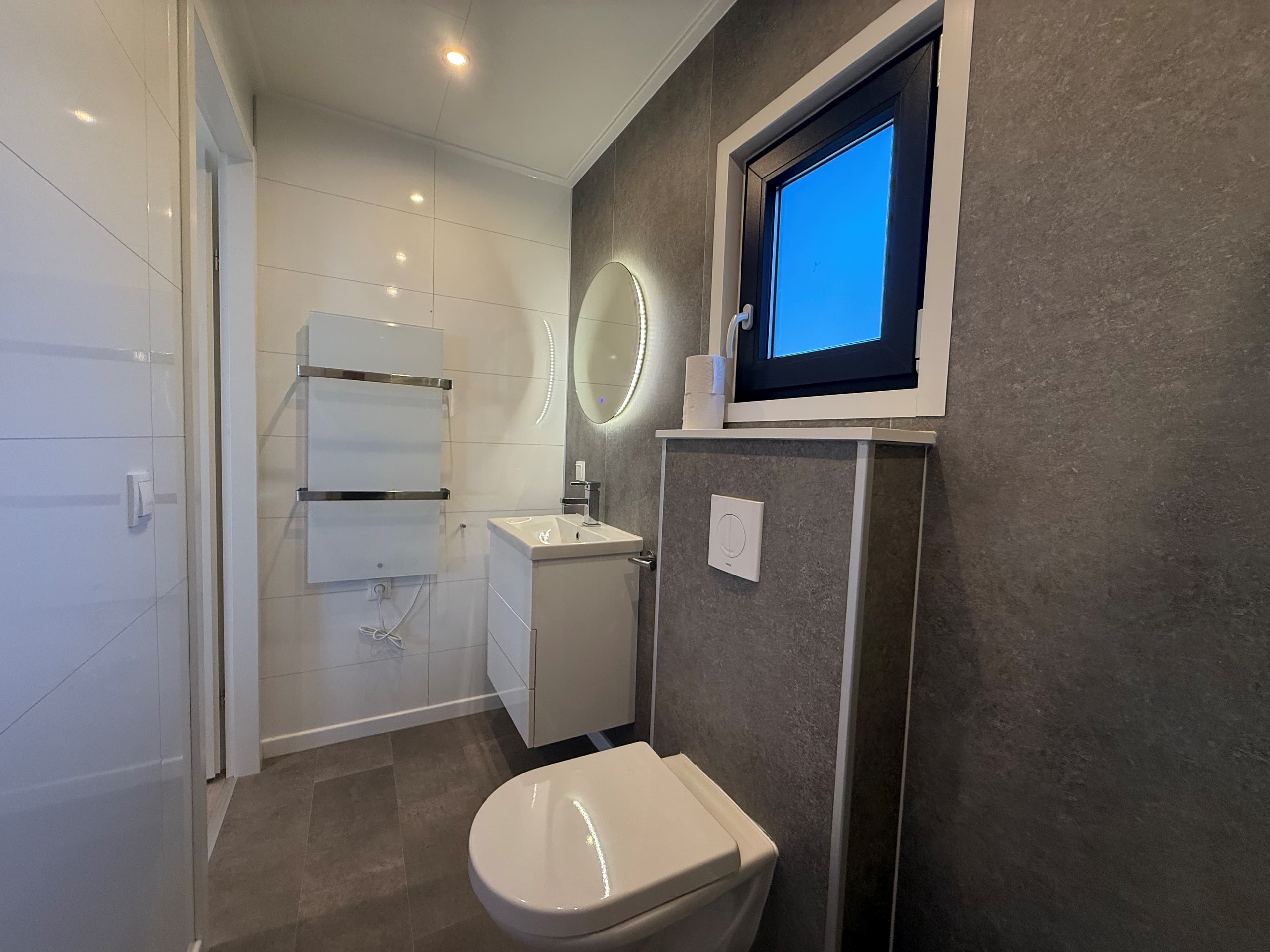 Moderne badkamer met wandtegels, een wastafel met spiegel en een toilet, raam met natuurlijke lichtinval.