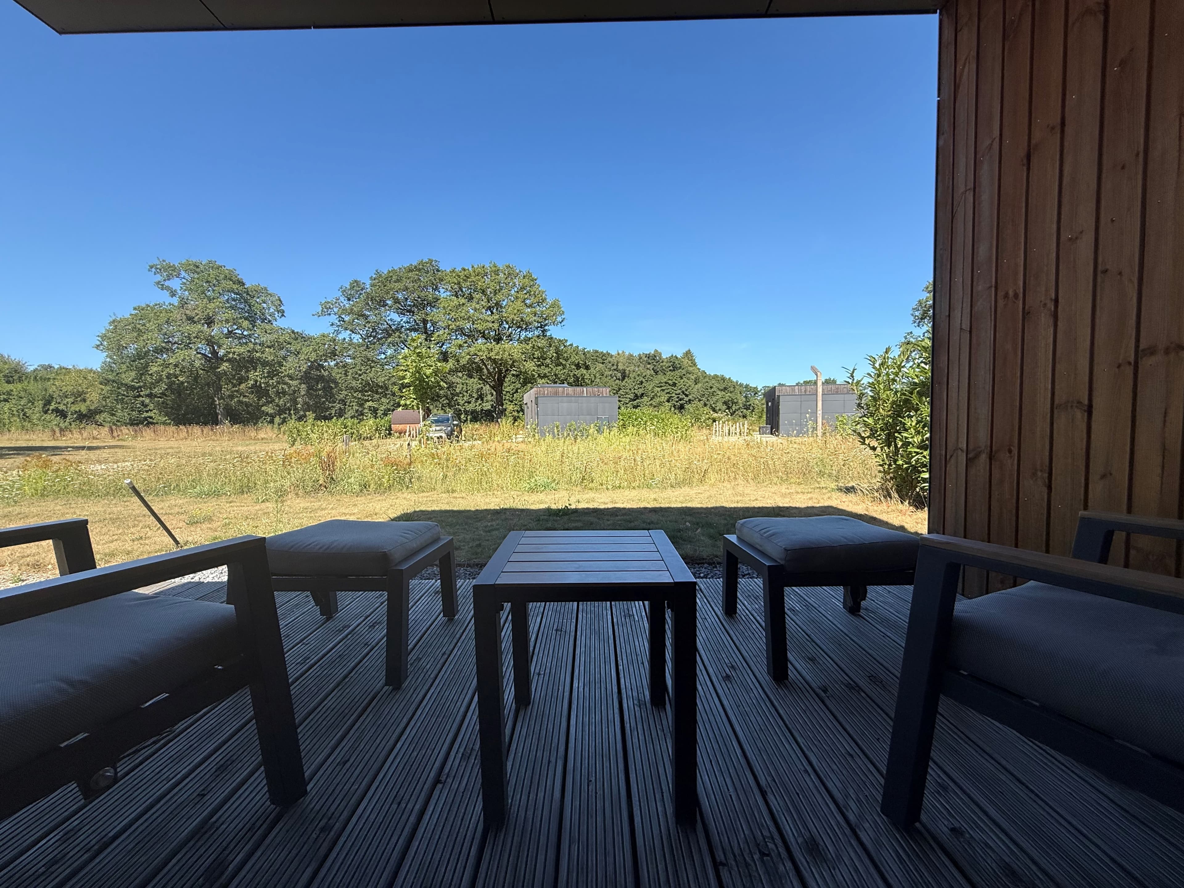Terras met houten vlonder en tuinmeubels, uitzicht op een groene wei met bomen en landerijen op de achtergrond