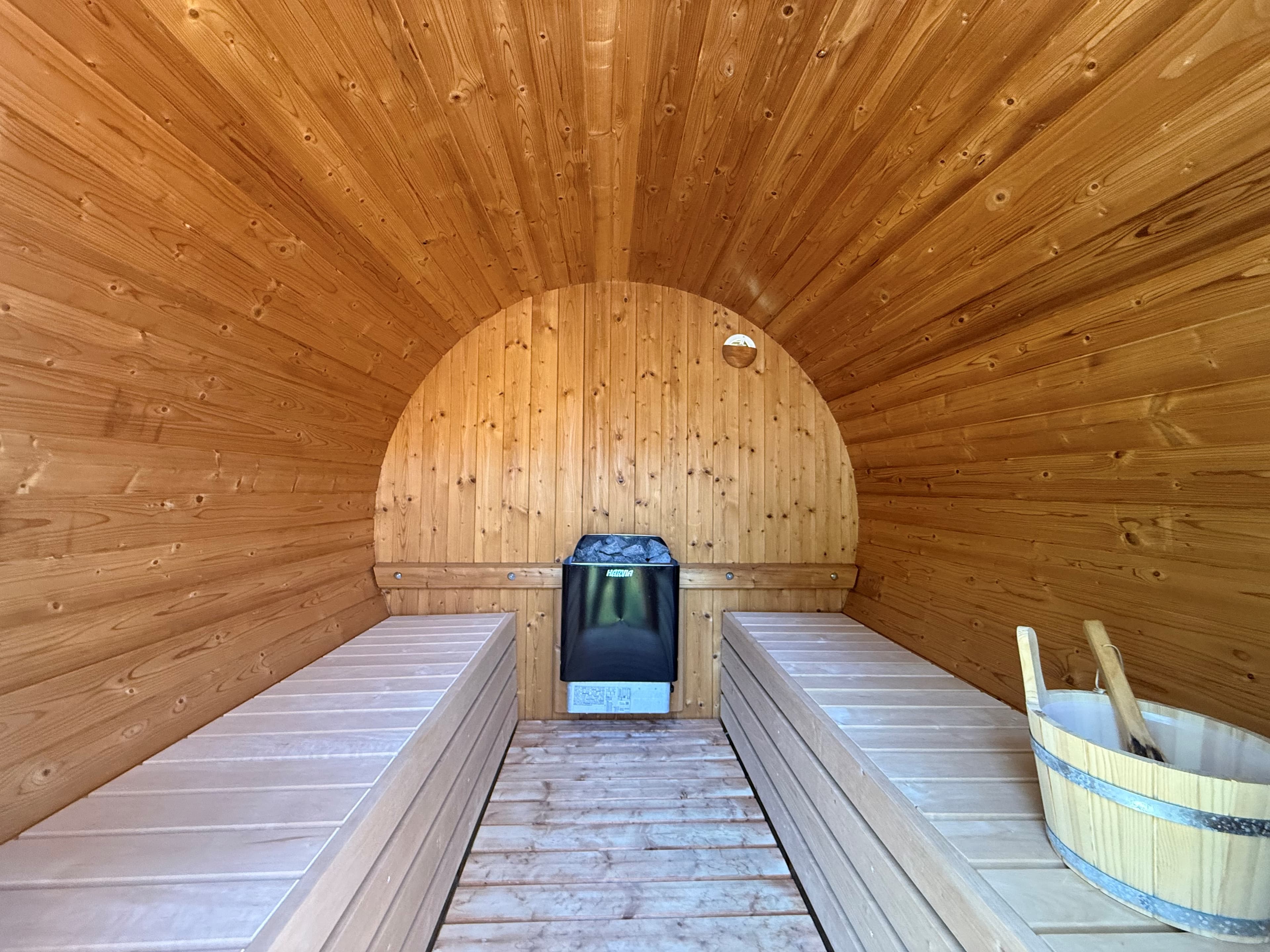 Interieur van een sauna met houten wandbekleding, benches aan weerszijden en een kachel in het midden.