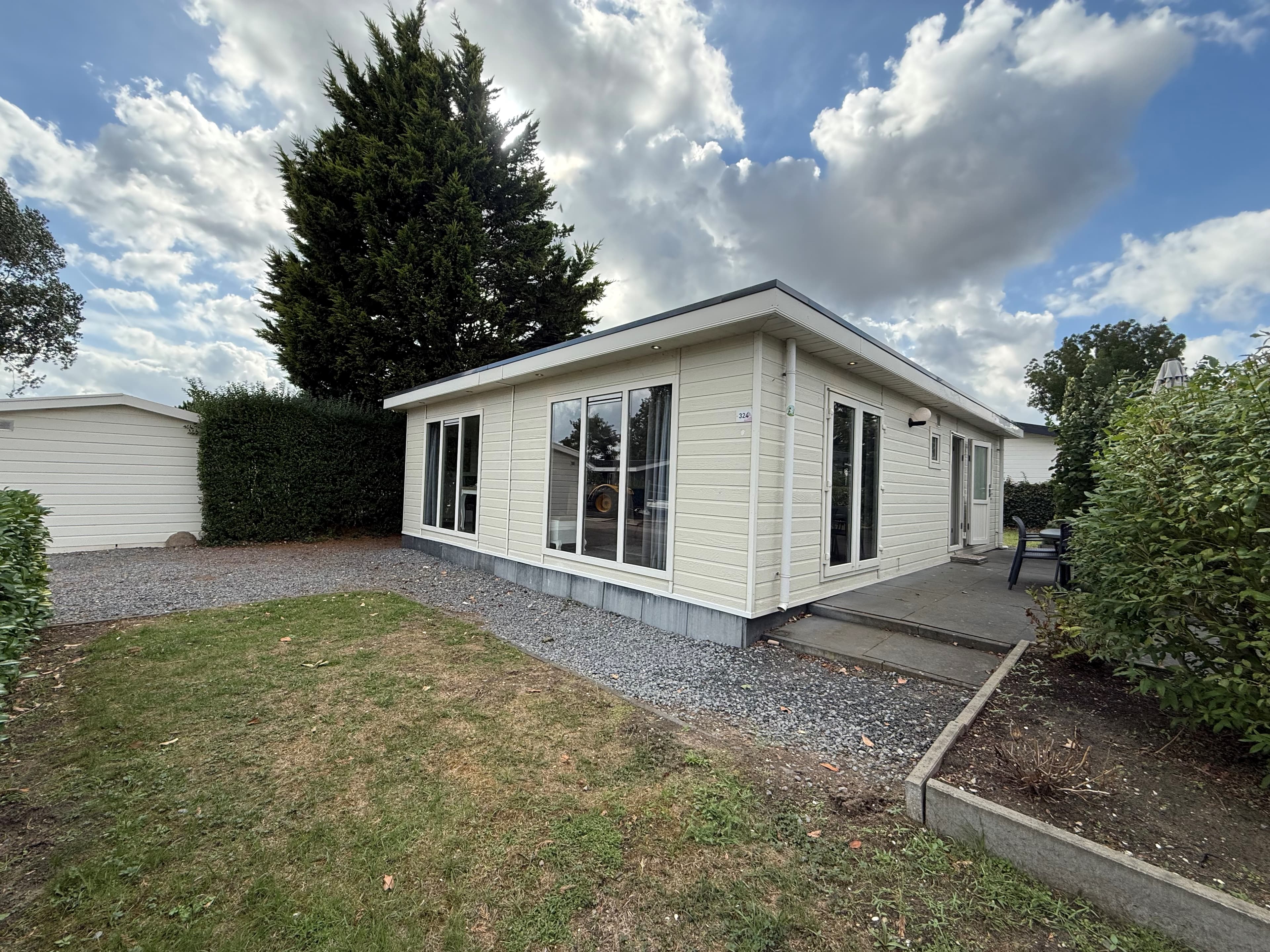 Moderne recreatiewoning met grote ramen, omgeven door gras en bomen, aan een gravelpad bij EuroParcs De Biesbosch
