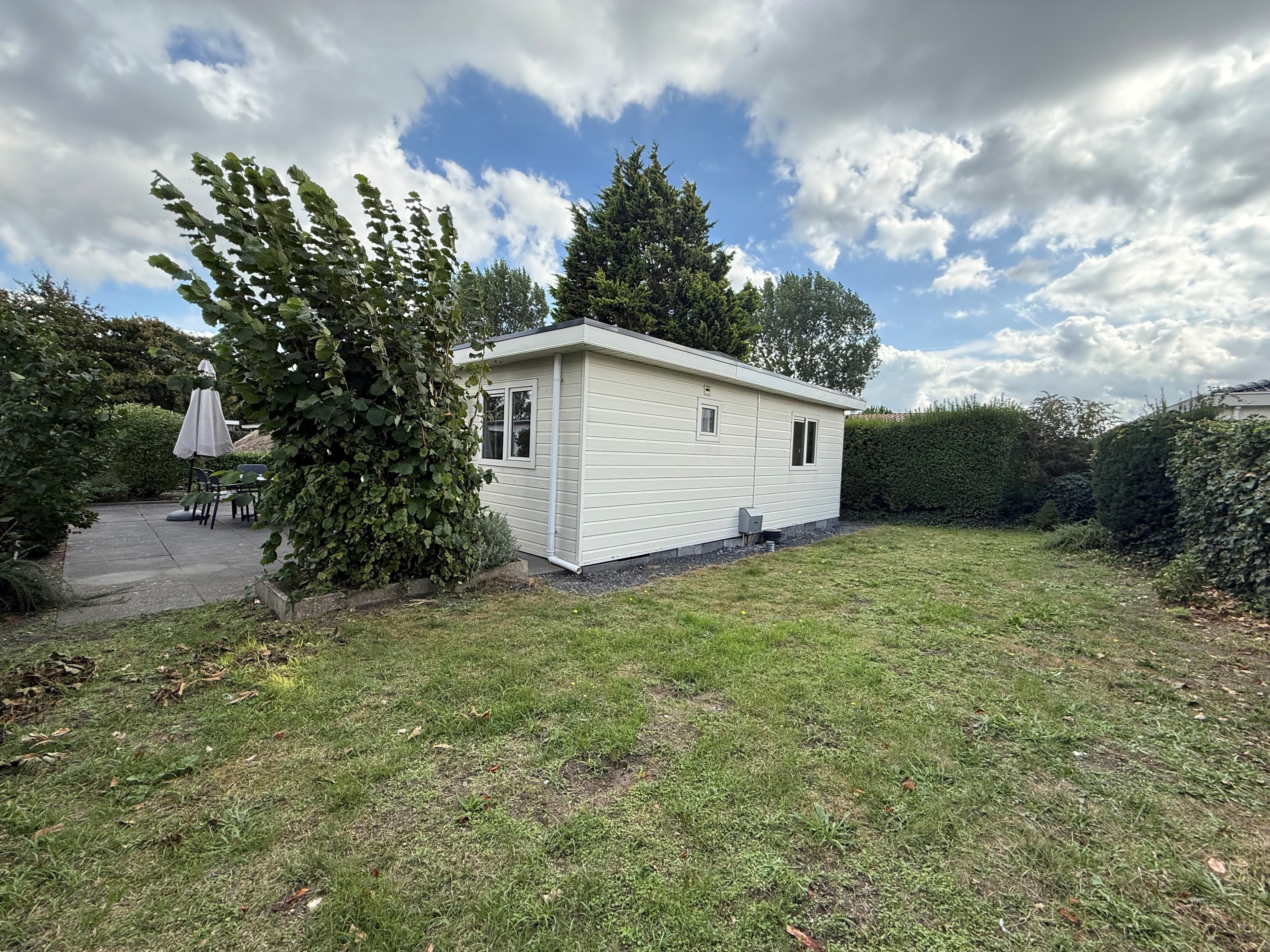 Recreatiewoning aan de rand van een groene tuin met gras en struiken, deels verhard terras zichtbaar achterin