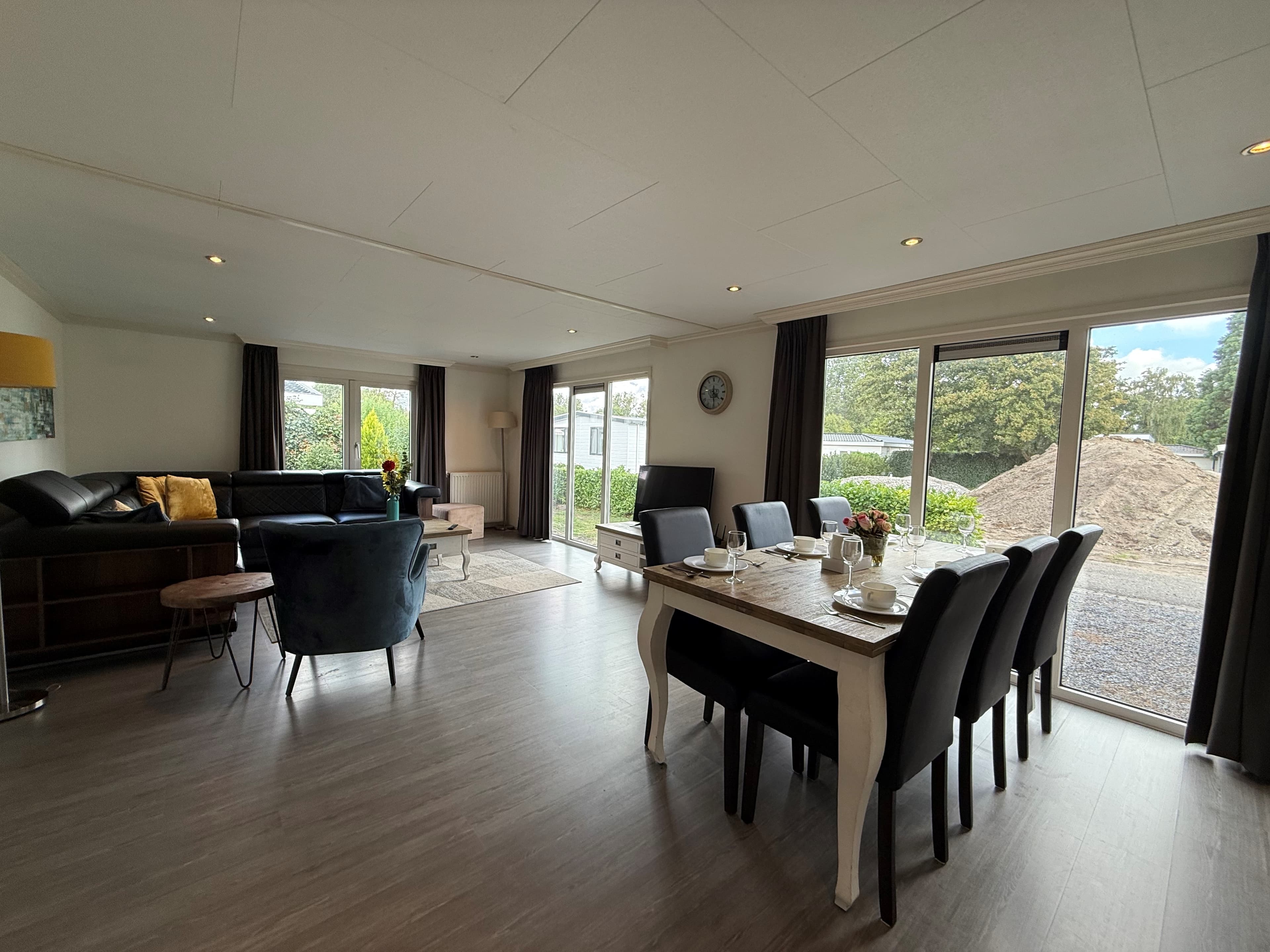 Moderne woonkamer met grote ramen, zithoek en een eettafel met stoelen aan de andere kant van de ruimte