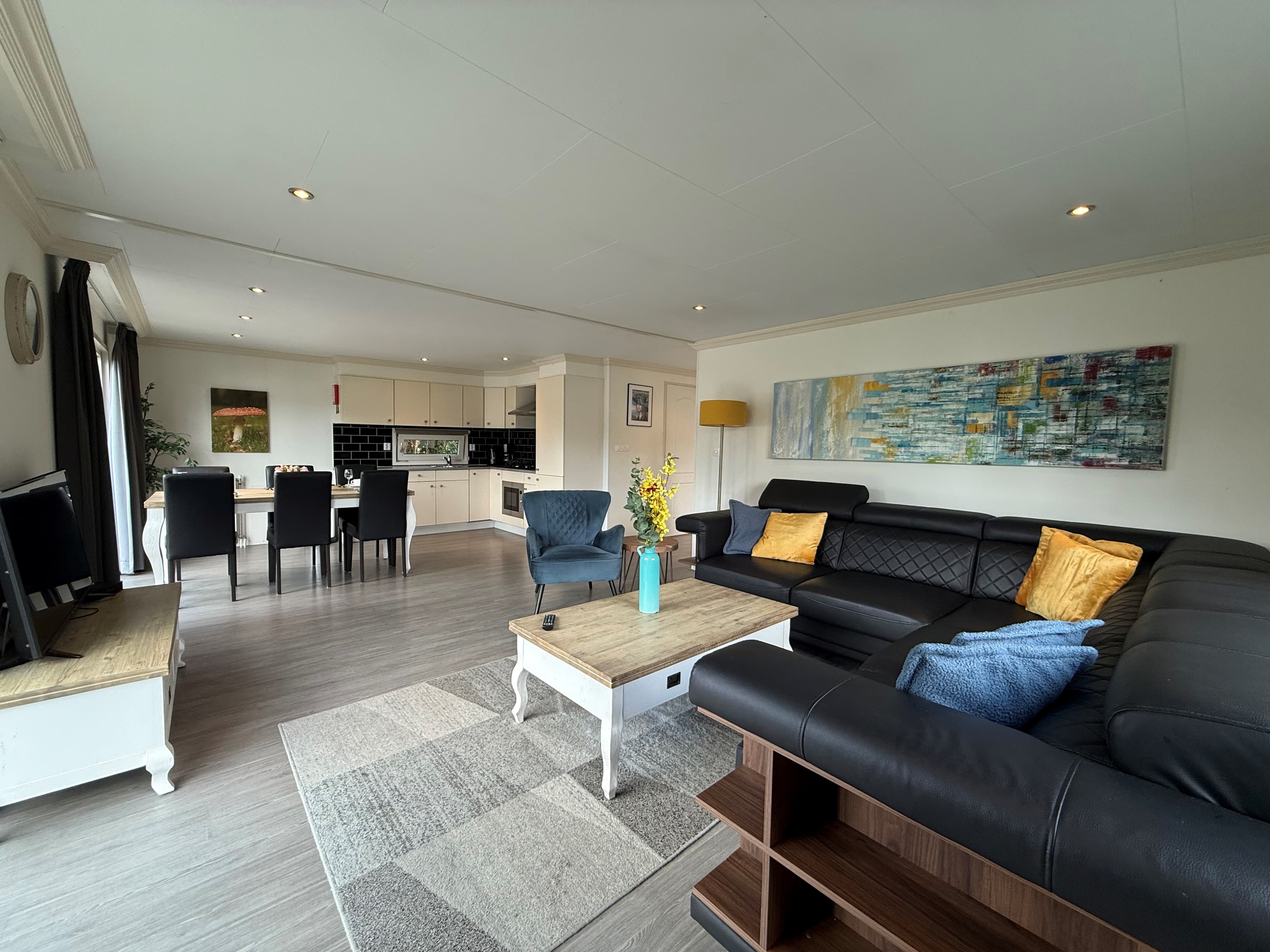 Moderne woonkamer met zwarte bank, eettafel, keuken en kunst aan de muur in een recreatiewoning