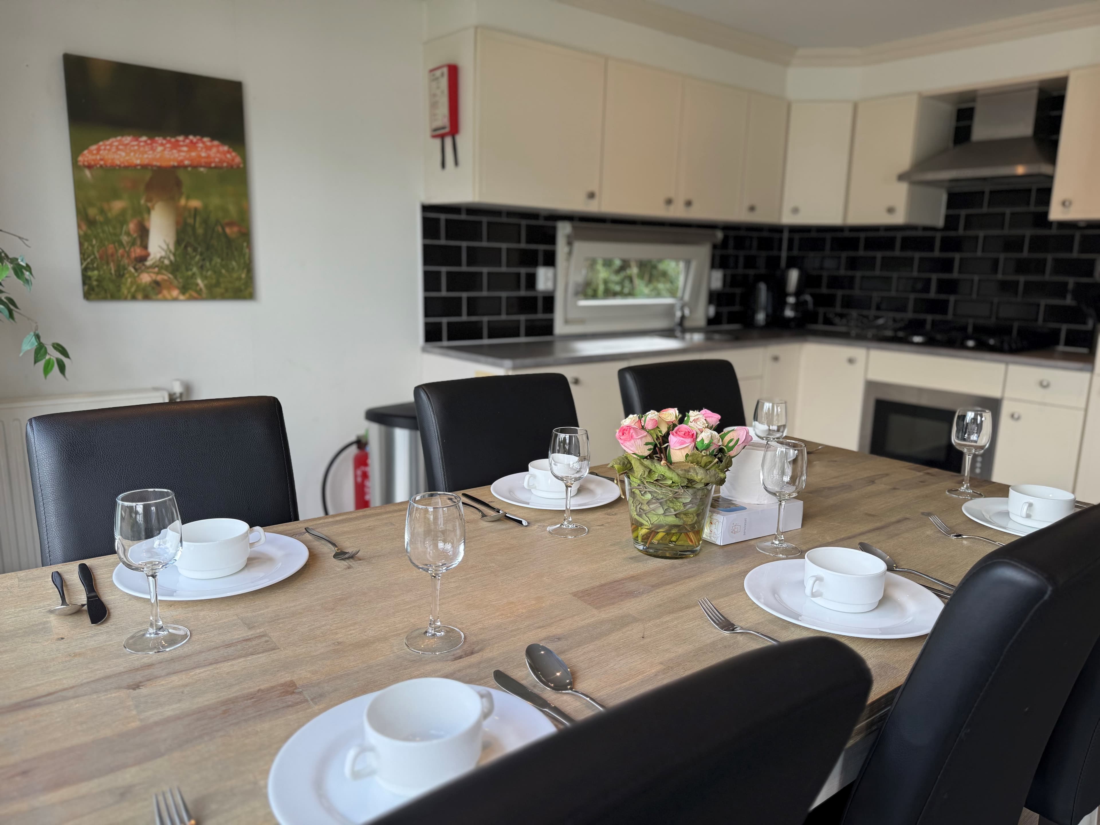 Eettafel met borden en glazen, moderne keuken met zwarte achterwand en een schilderij van een paddenstoel aan de muur