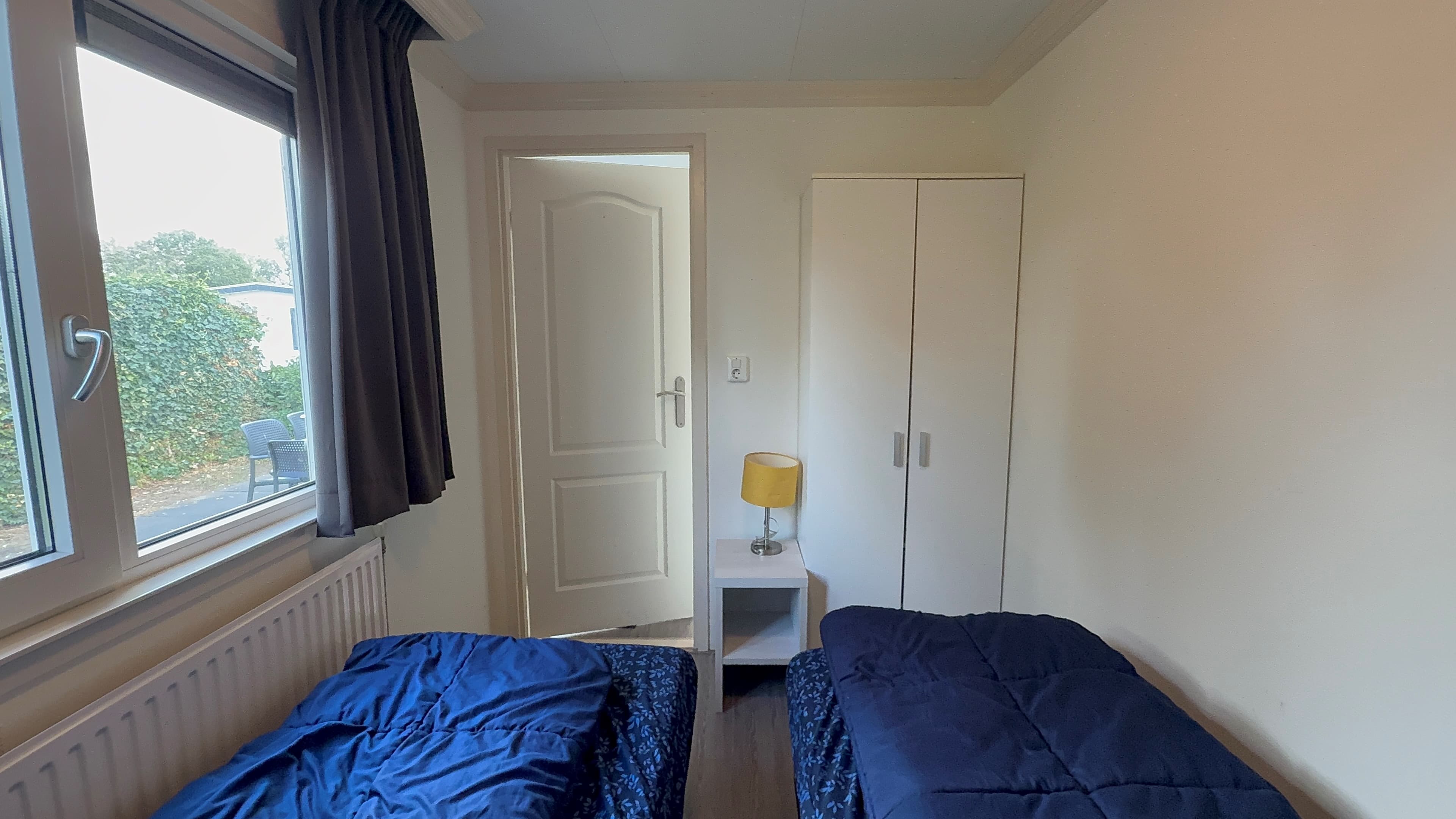 Slaapkamer met twee bedden, een kast, nachtkastje en raam met uitzicht op de buitenruimte
