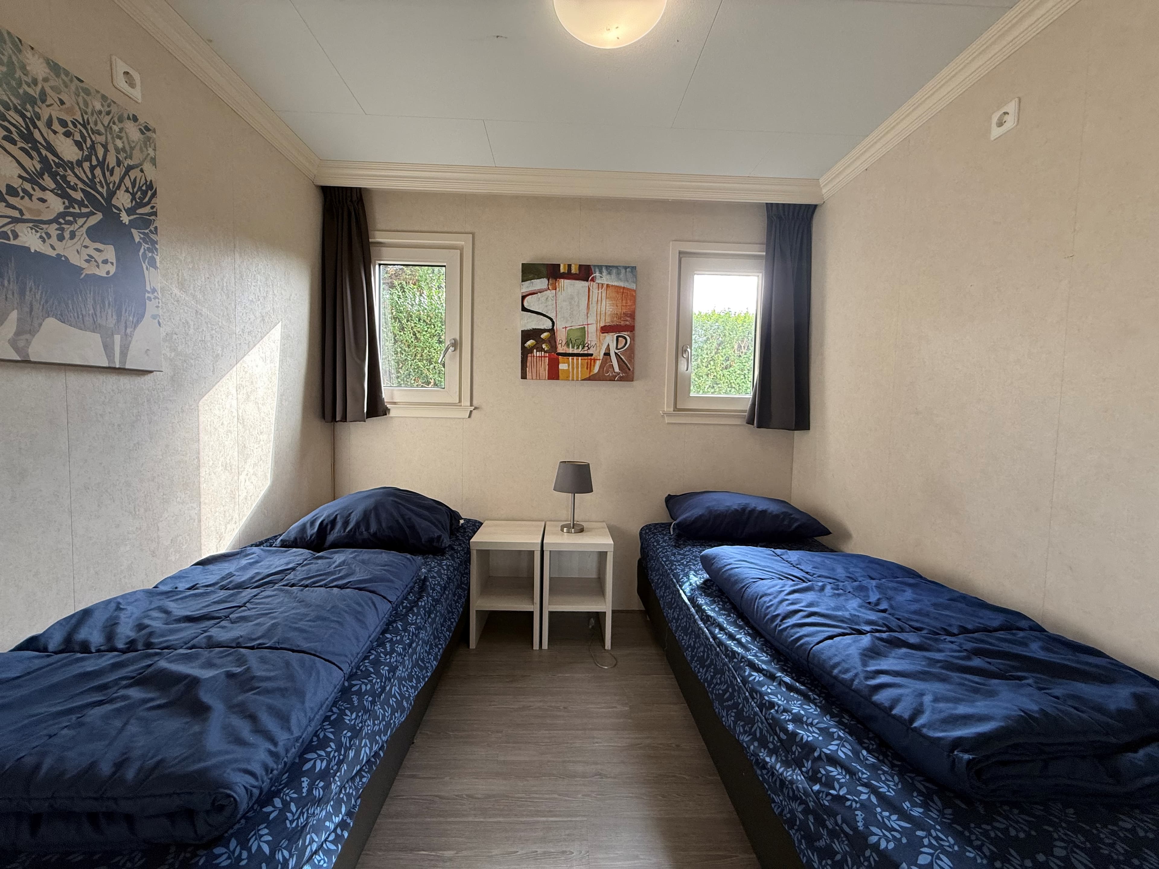 Slaapkamer met twee eenpersoonsbedden, een nachtkastje en kunst aan de muur. Raam met gordijnen aan beide zijden.