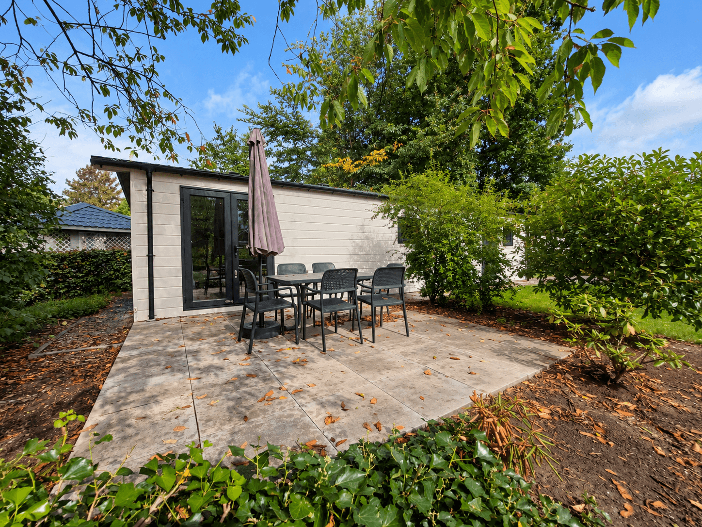 Terras met tuinmeubilair en parasol naast een recreatiewoning omringd door groen in een rustige omgeving