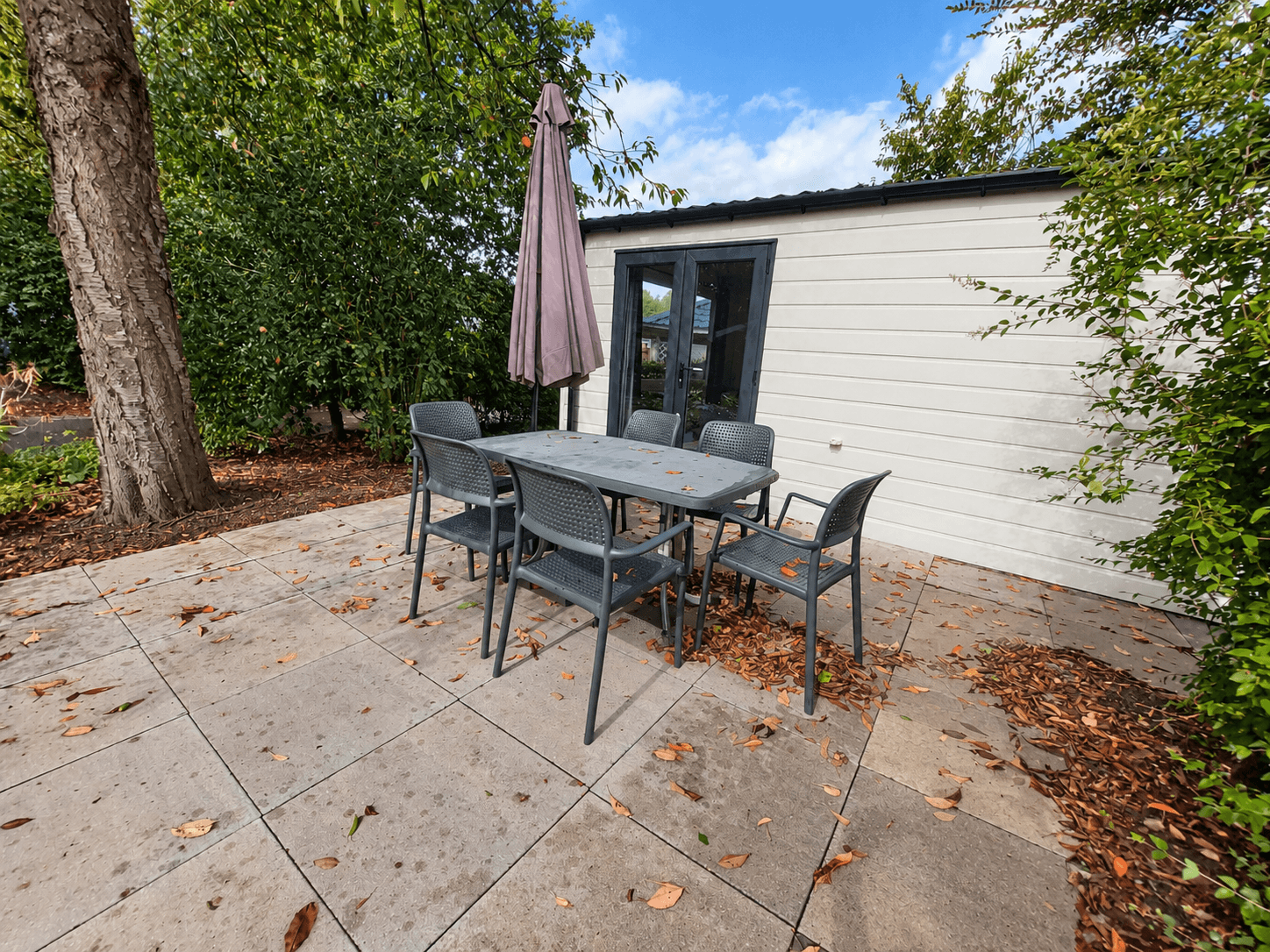 Terras met een tafel en vier stoelen, omringd door groen en een parasol, naast een recreatiewoning.