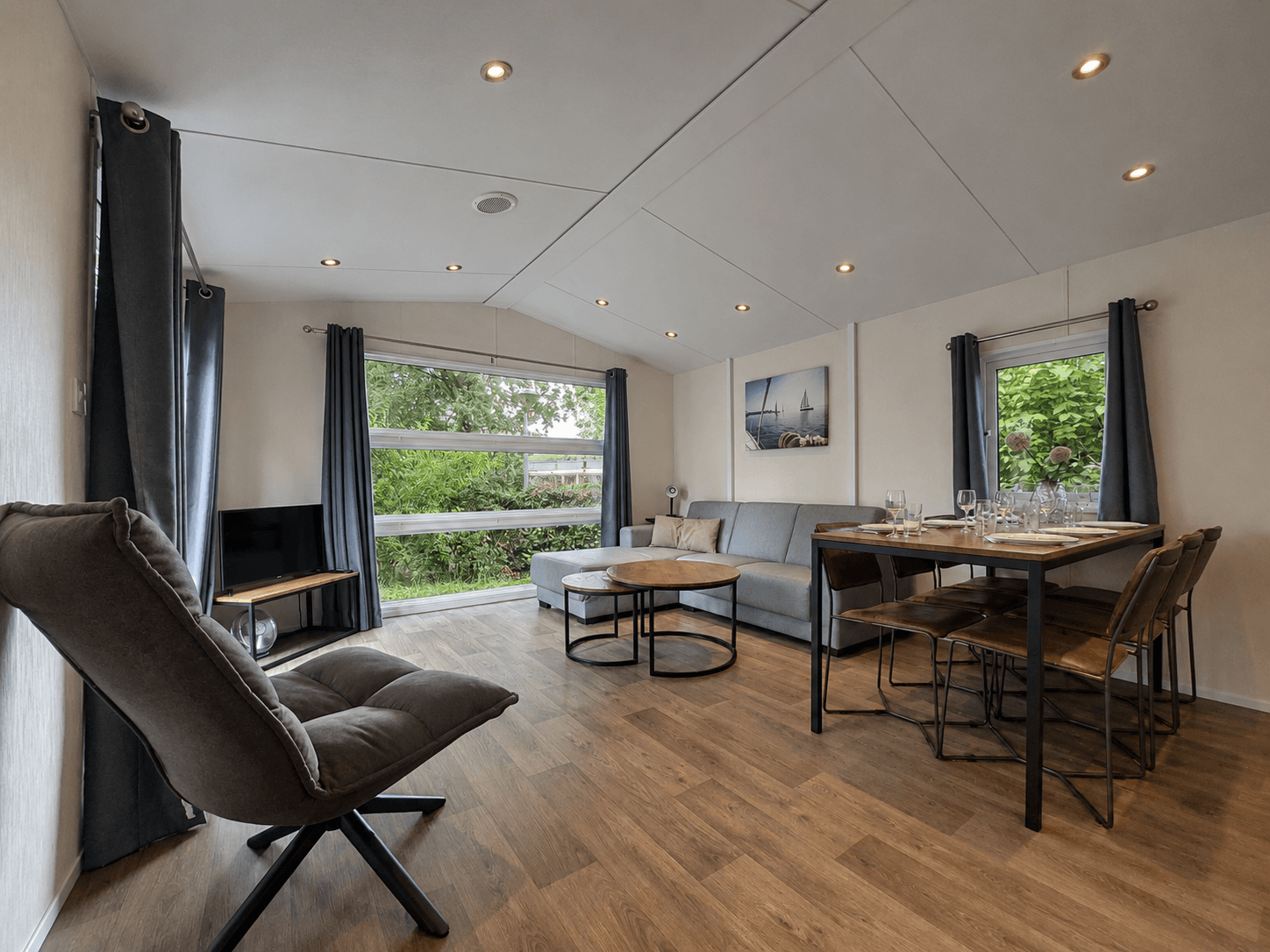 Woonkamer met zithoek, eettafel, grote ramen en moderne inrichting, uitzicht op groene omgeving en natuurlicht