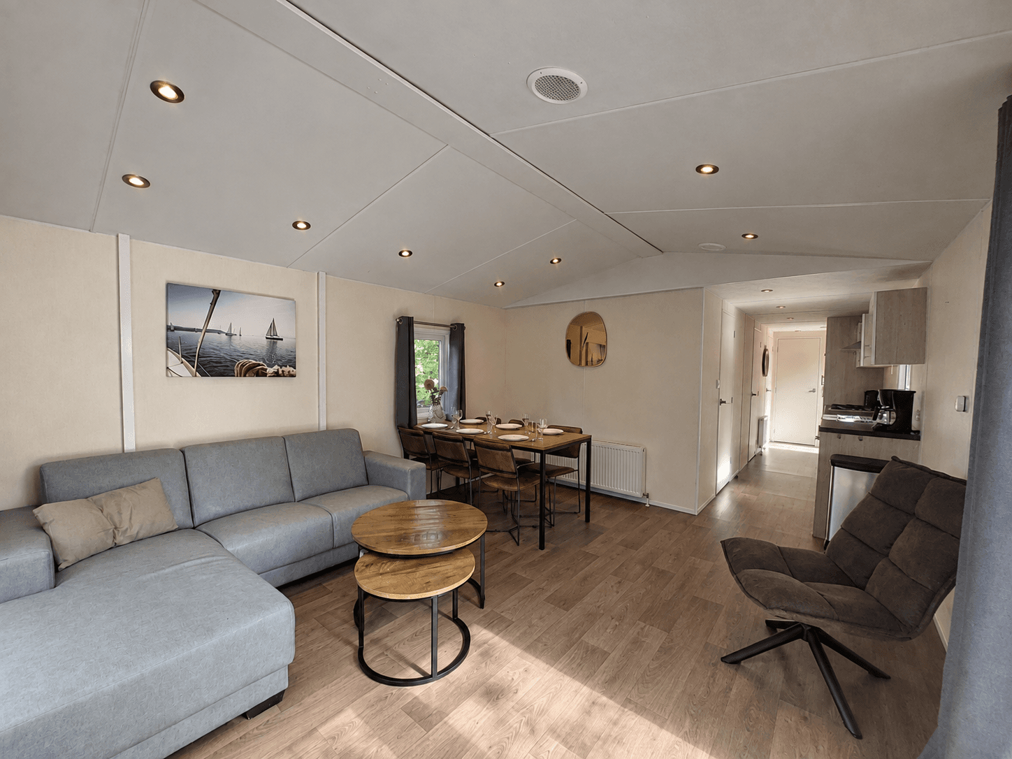Moderne woonkamer met zithoek, eettafel en open keuken, grote ramen zorgen voor een lichte uitstraling