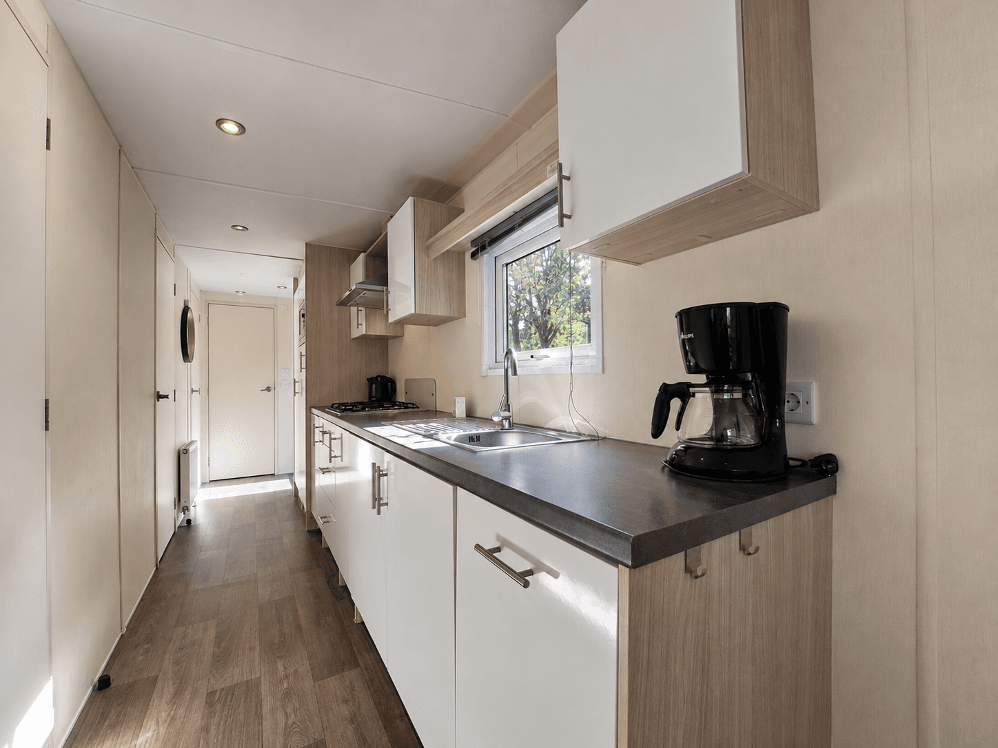 Keuken met modern keukenblad, kastjes, kookplaat, oven en koffiezetapparaat in een recreatiewoning.