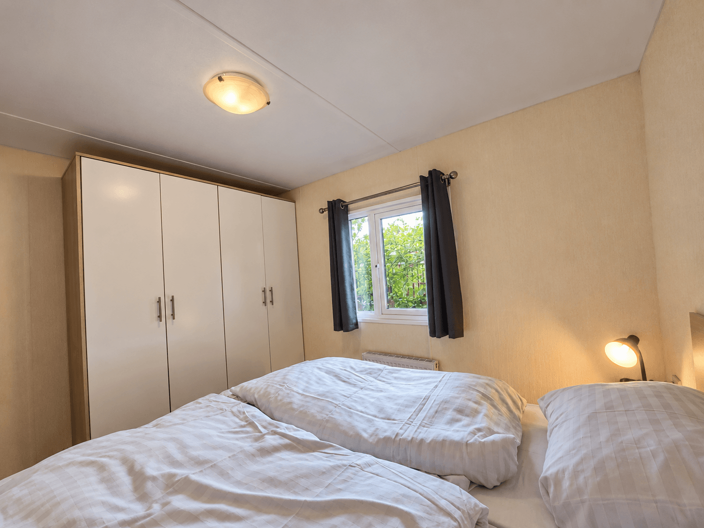 Slaapkamer met twee eenpersoonsbedden, een grote kast en een raam met uitzicht op groene begroeiing.
