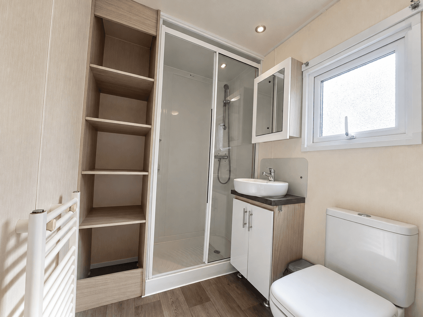 Moderne badkamer met douchecabine, wastafel en toilet, voorzien van opbergkasten en een raam.
