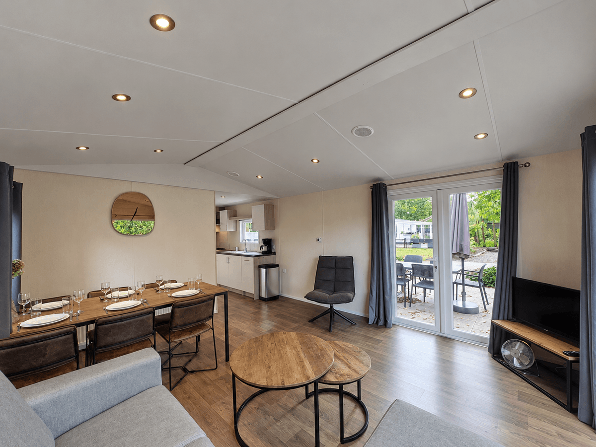 Moderne recreatiewoning met eetgedeelte, zithoek en openslaande deuren naar het terras met tuinmeubilair