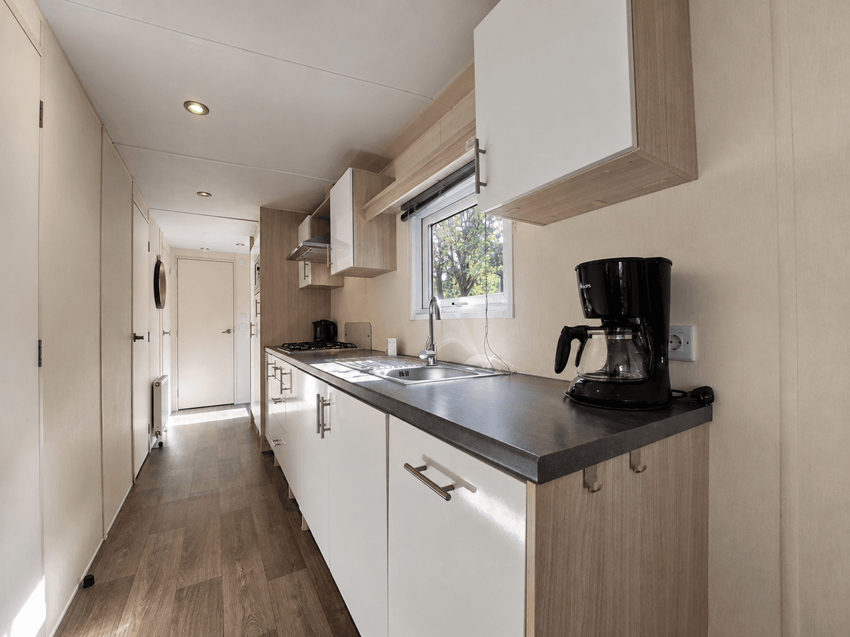 Keuken met modern keukenblad, kastjes, kookplaat, oven en koffiezetapparaat in een recreatiewoning.