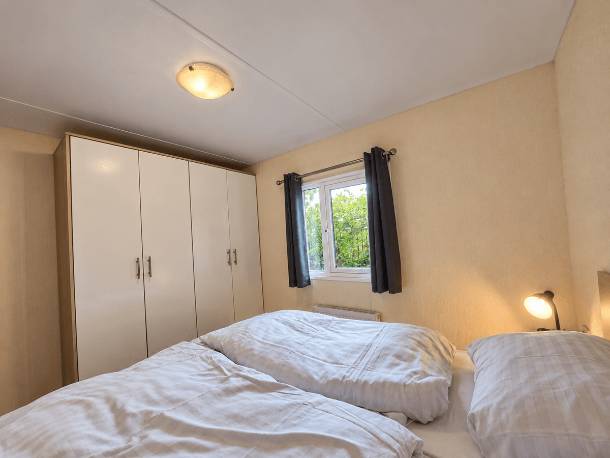 Slaapkamer met twee eenpersoonsbedden, een grote kast en een raam met uitzicht op groene begroeiing.