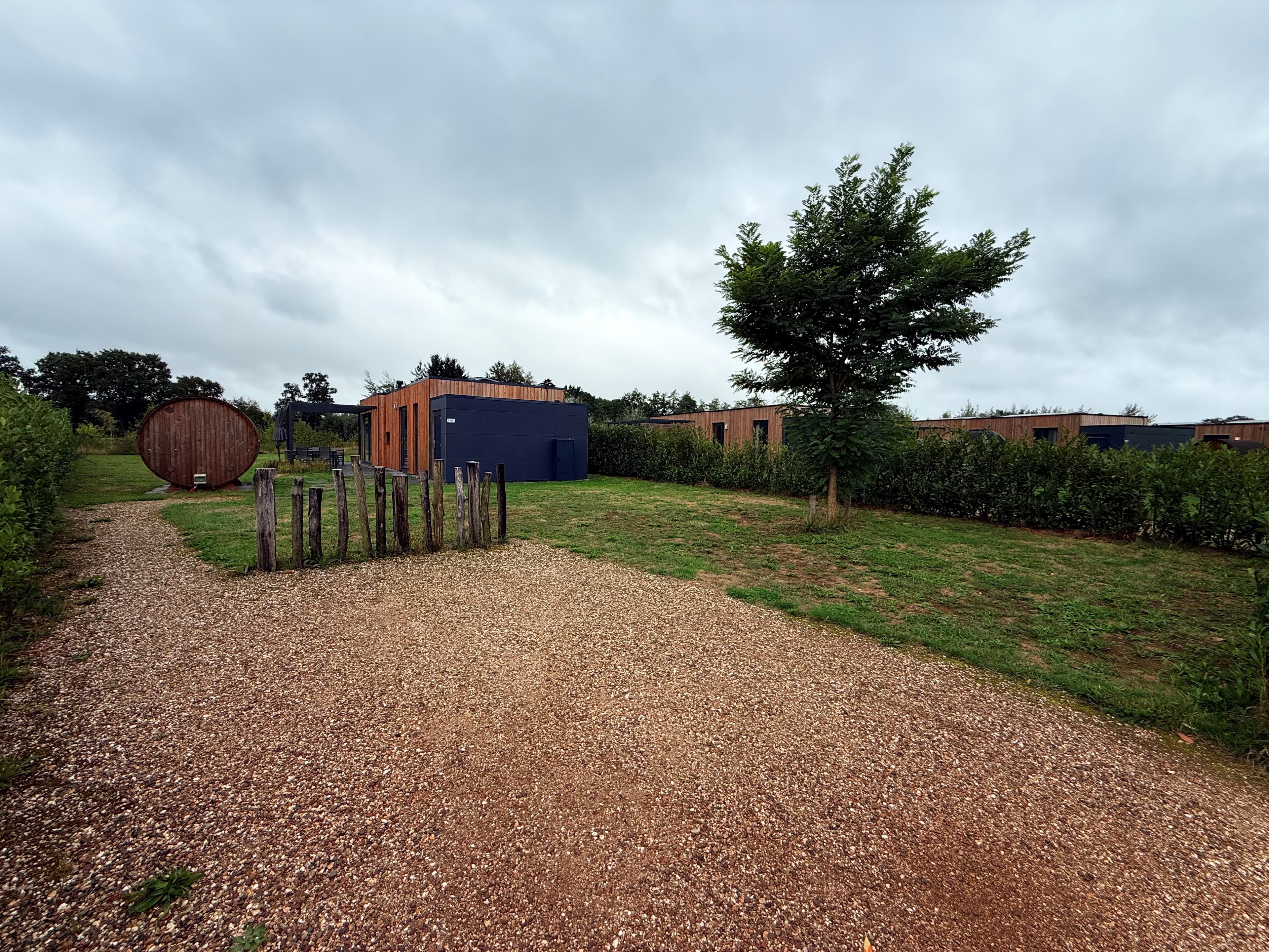 Groene buitenruimte met grindpad, houten vakantiewoningen en bomen in vakantiepark Hofparken Wiltershaar, Winterswijk Kotten