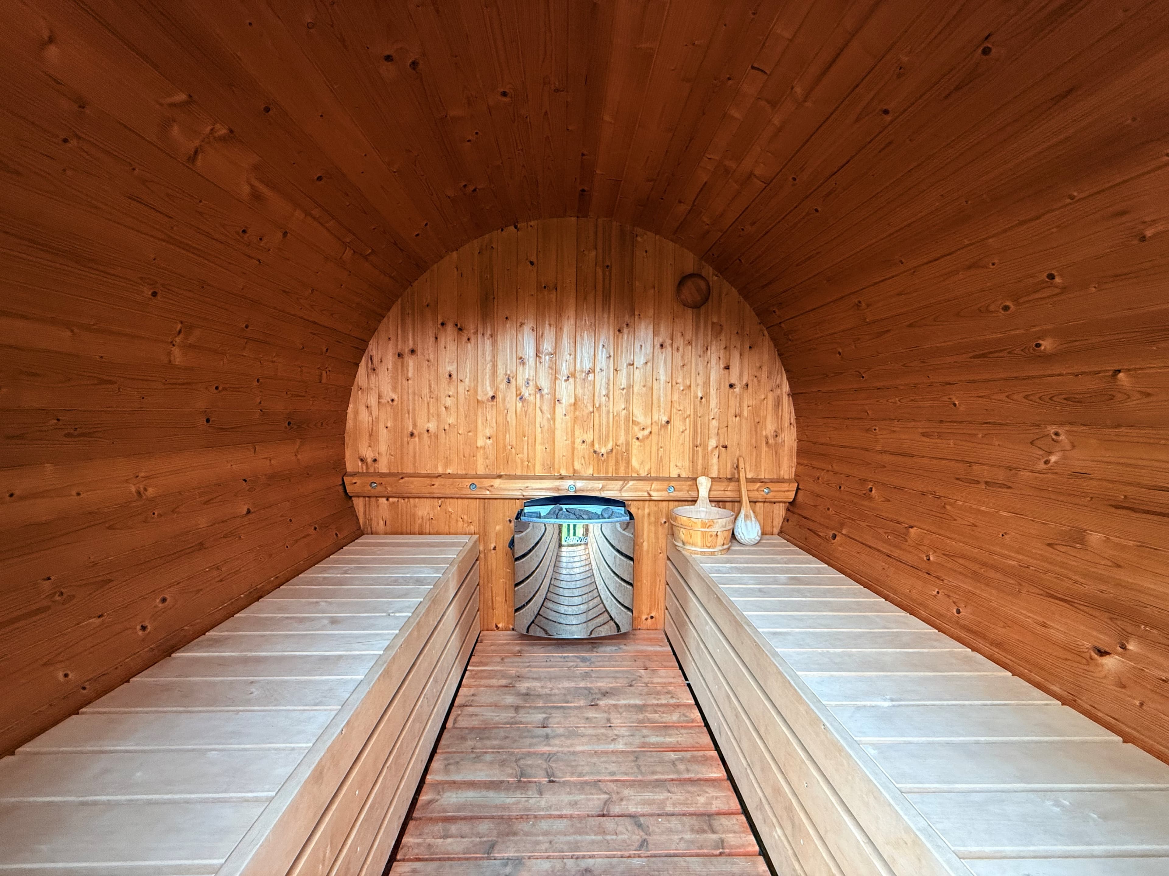 Binnenkant van een sauna met houten wanden, banken aan weerszijden en een haard in het midden.