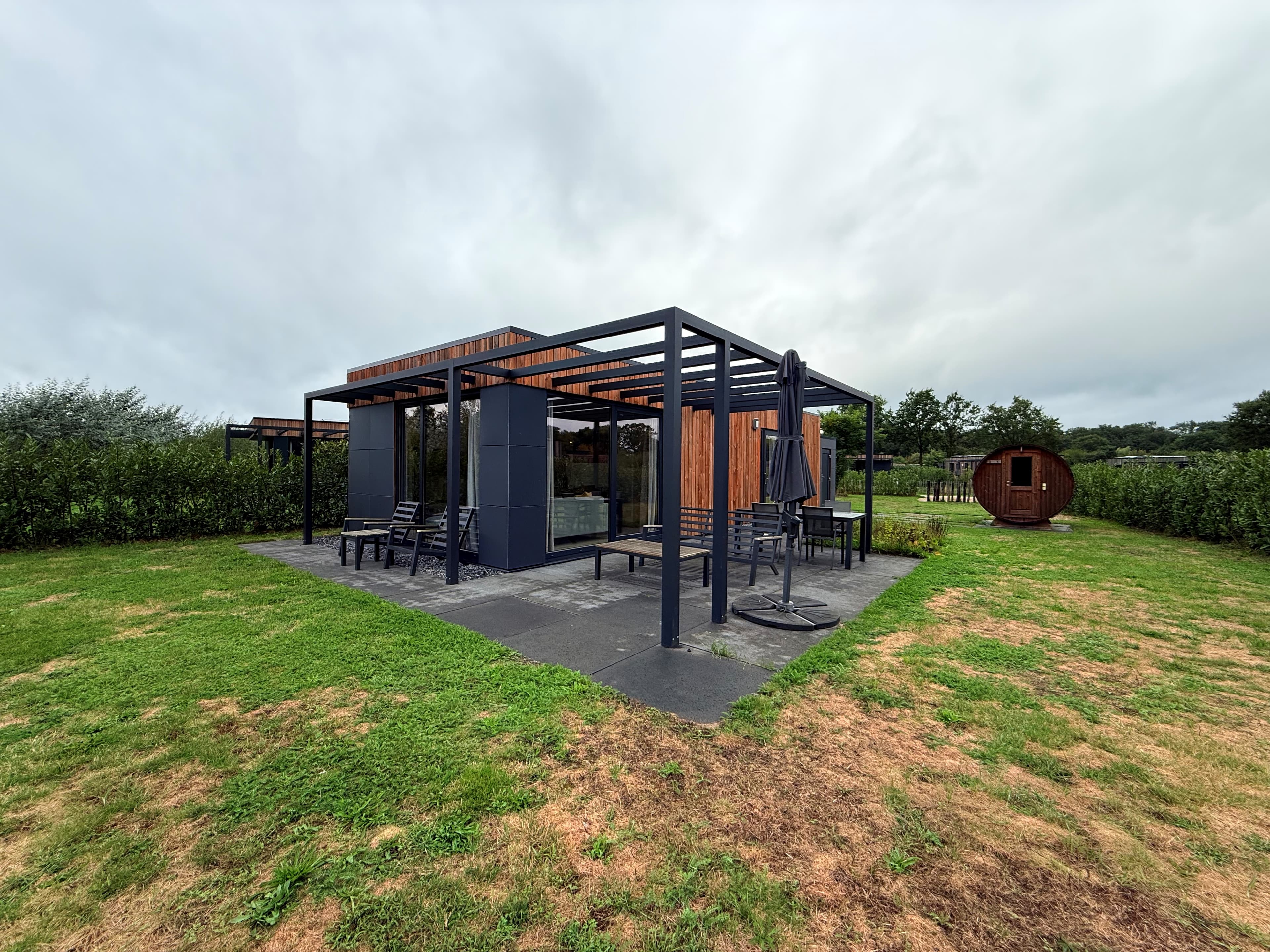 Recreatiewoning met overdekt terras en tuin, omgeven door gras en groen in Vakantiepark Hofparken Wiltershaar.