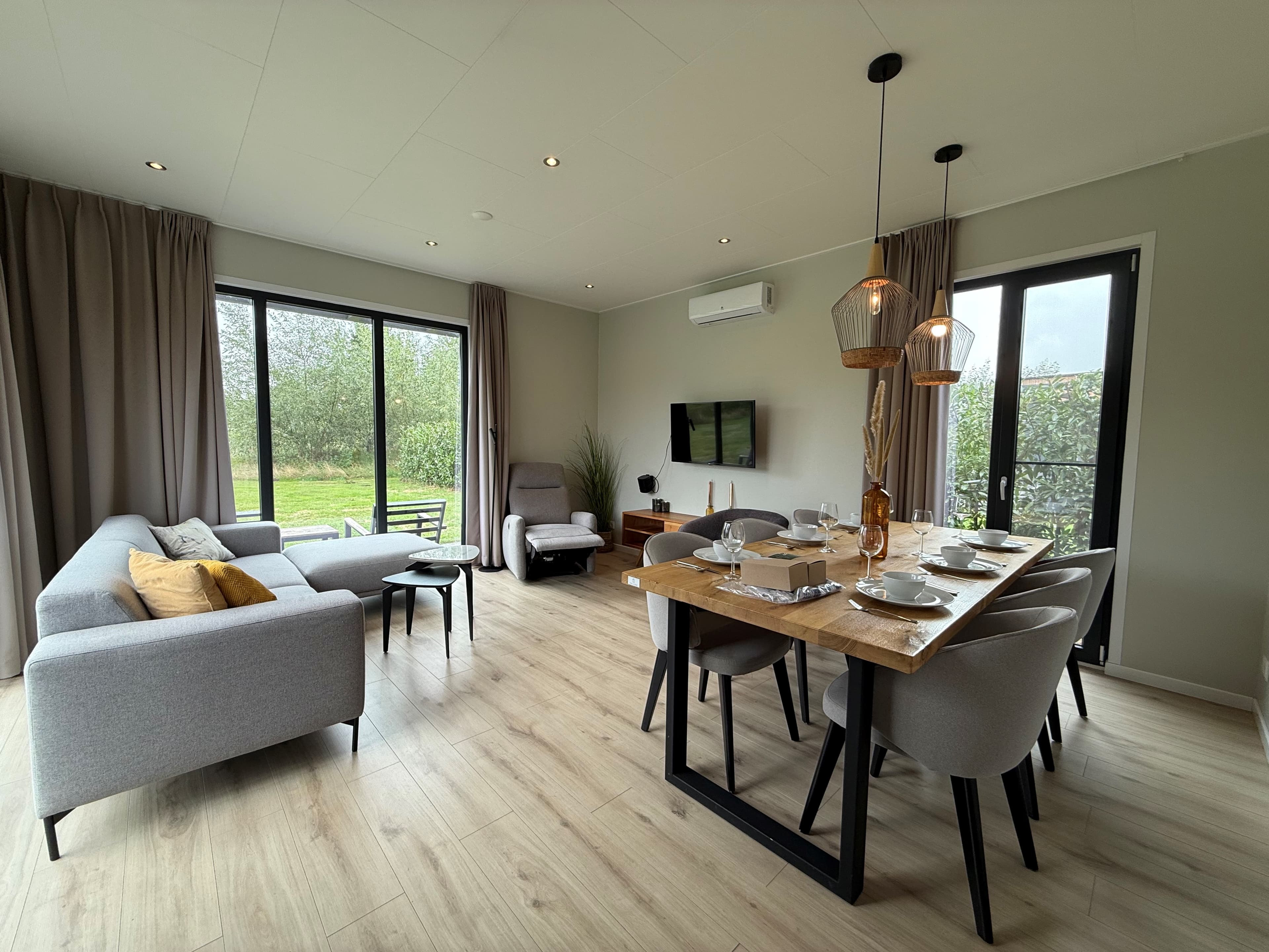 Moderne woonkamer met zithoek en eettafel, grote ramen met uitzicht op de groene omgeving en lichte inrichting