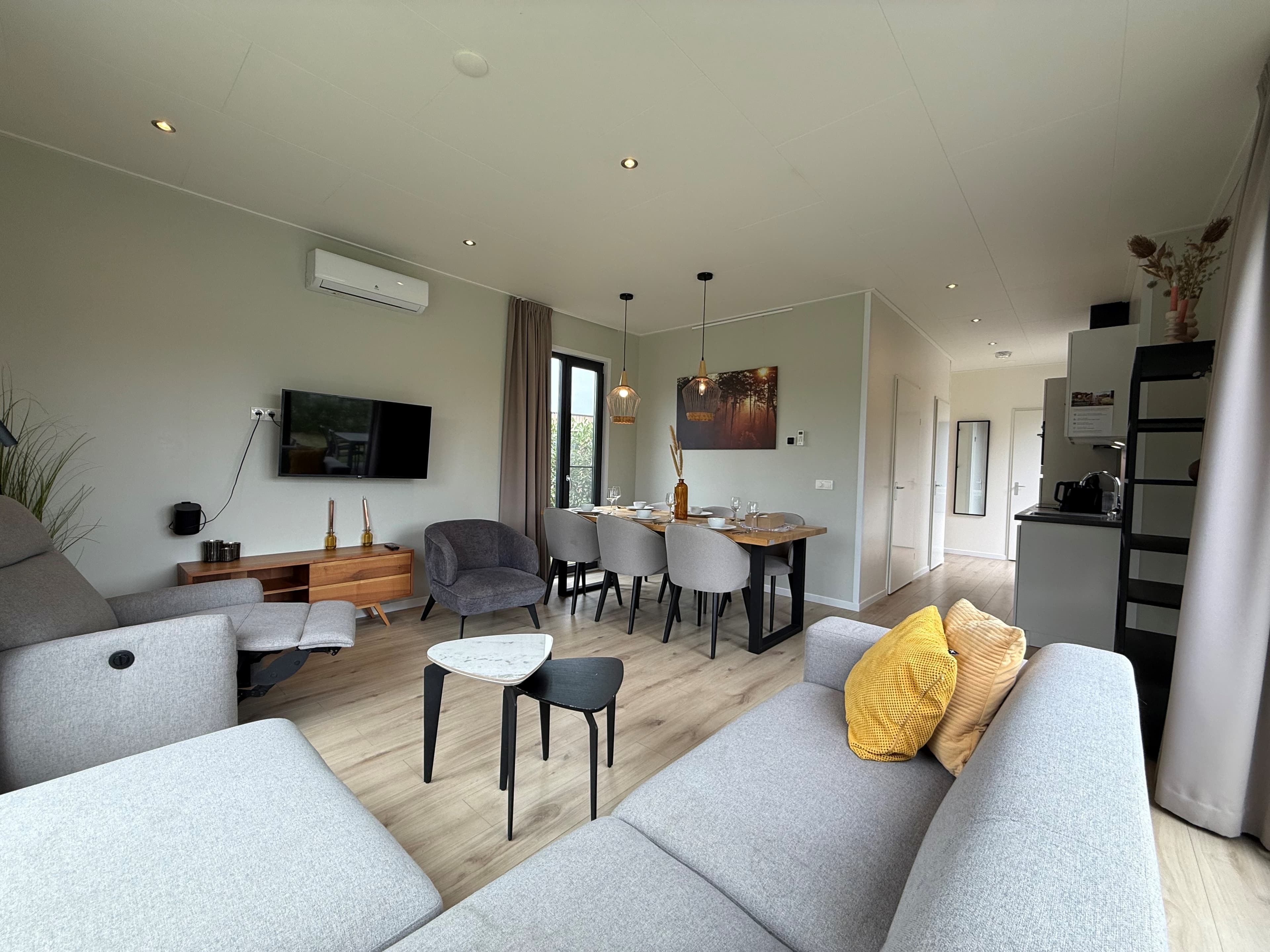 Moderne woonkamer met zithoek, eettafel en open keuken in een recreatiewoning met grote ramen en lichte inrichting