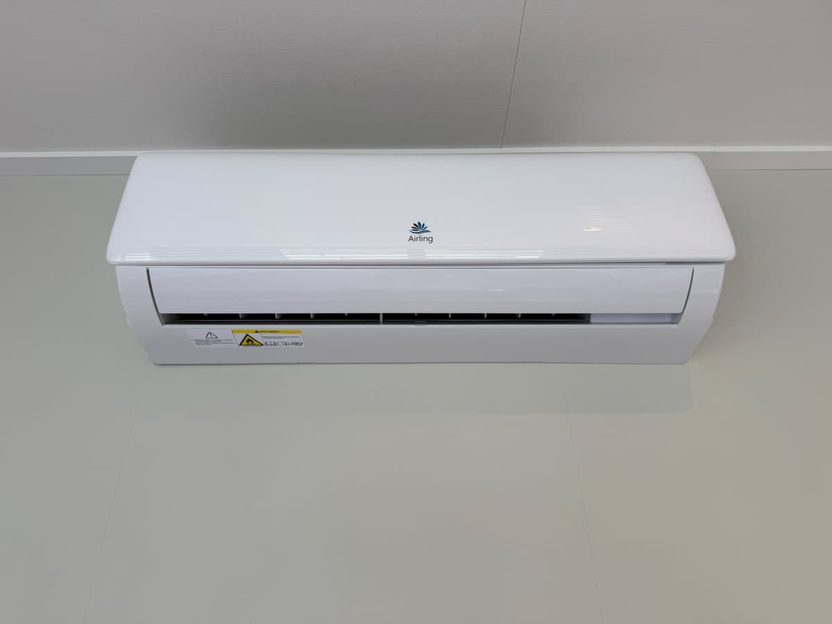Witte airconditioningseenheid tegen een lichte muur met een neutrale vloer in een binnenruimte.