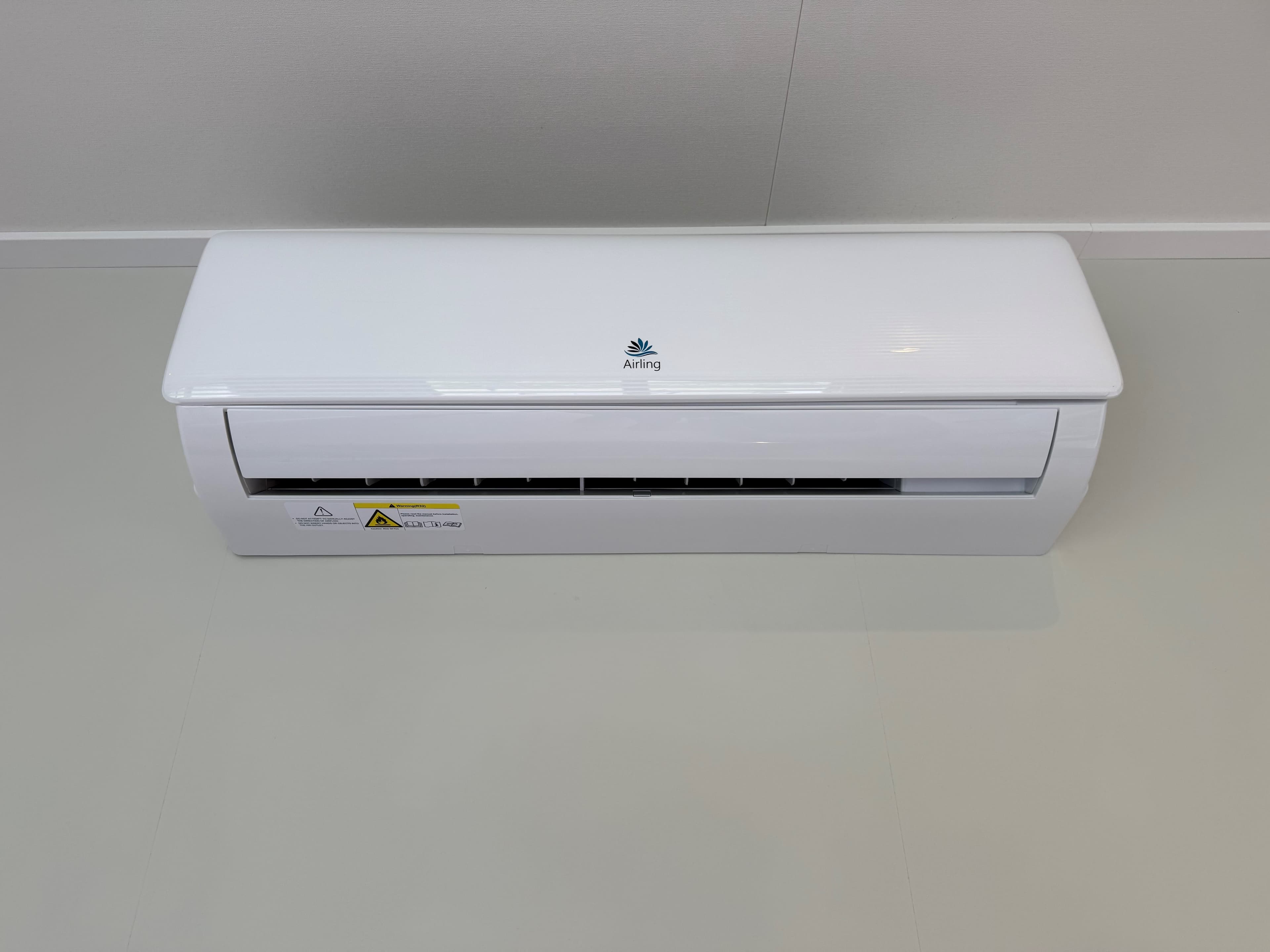 Witte airconditioningseenheid tegen een lichte muur met een neutrale vloer in een binnenruimte.