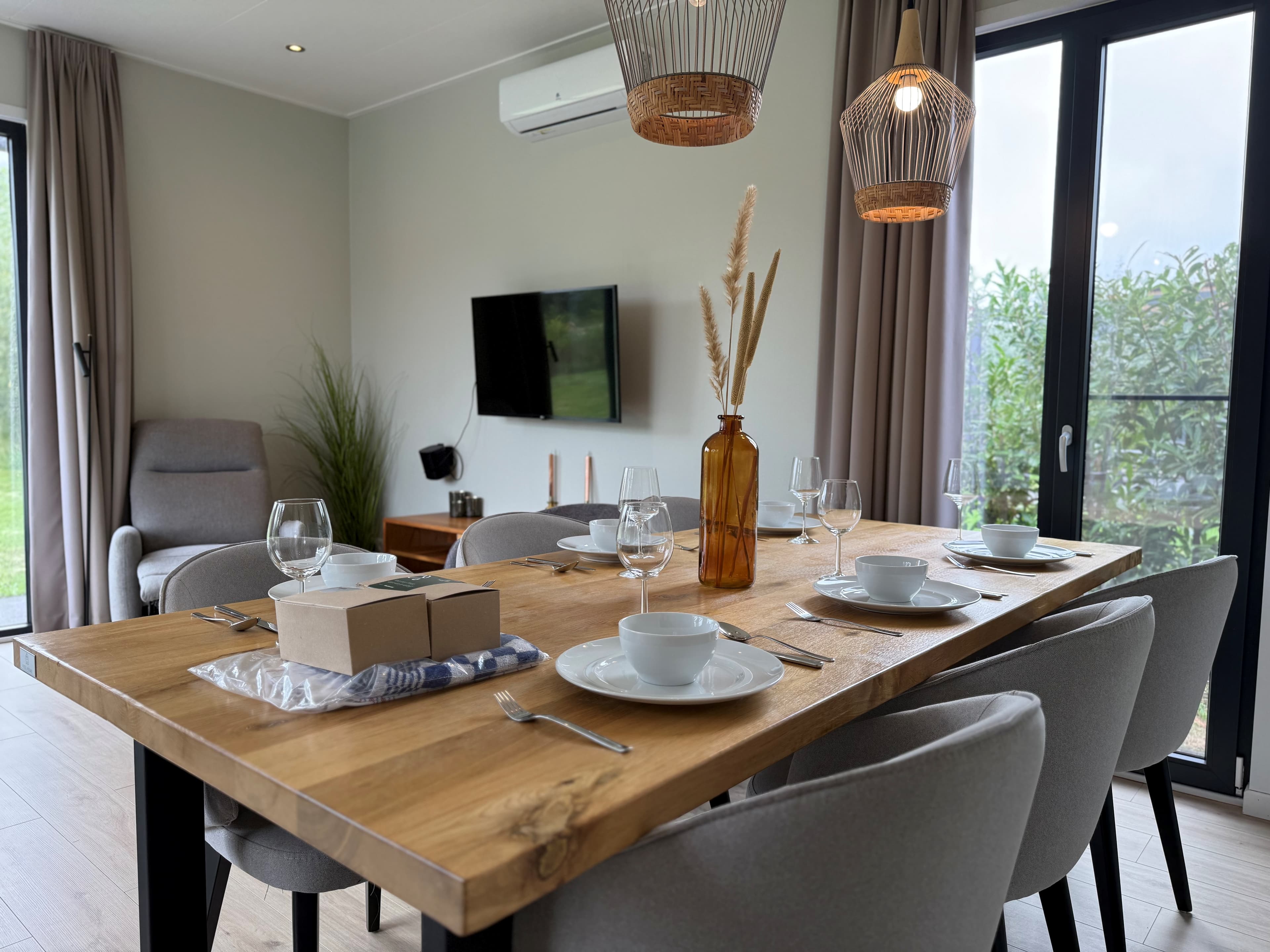 Eetgedeelte met een houten tafel, moderne stoelen, en een grote vaas met droogbloemen in een recreatiewoning.