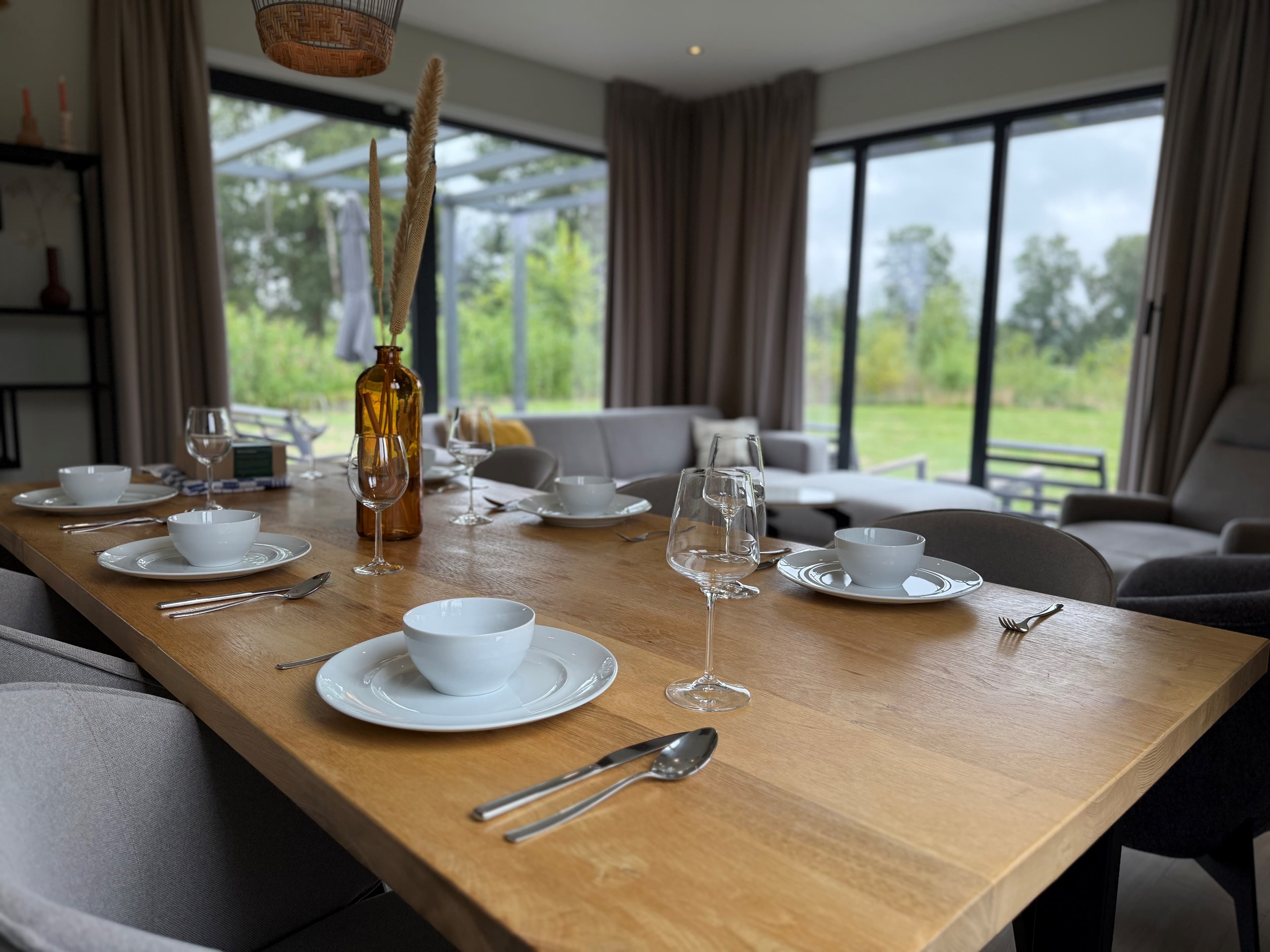 Eetkamertafel met borden en glazen, omringd door comfortabele stoelen en uitzicht op een groene omgeving.