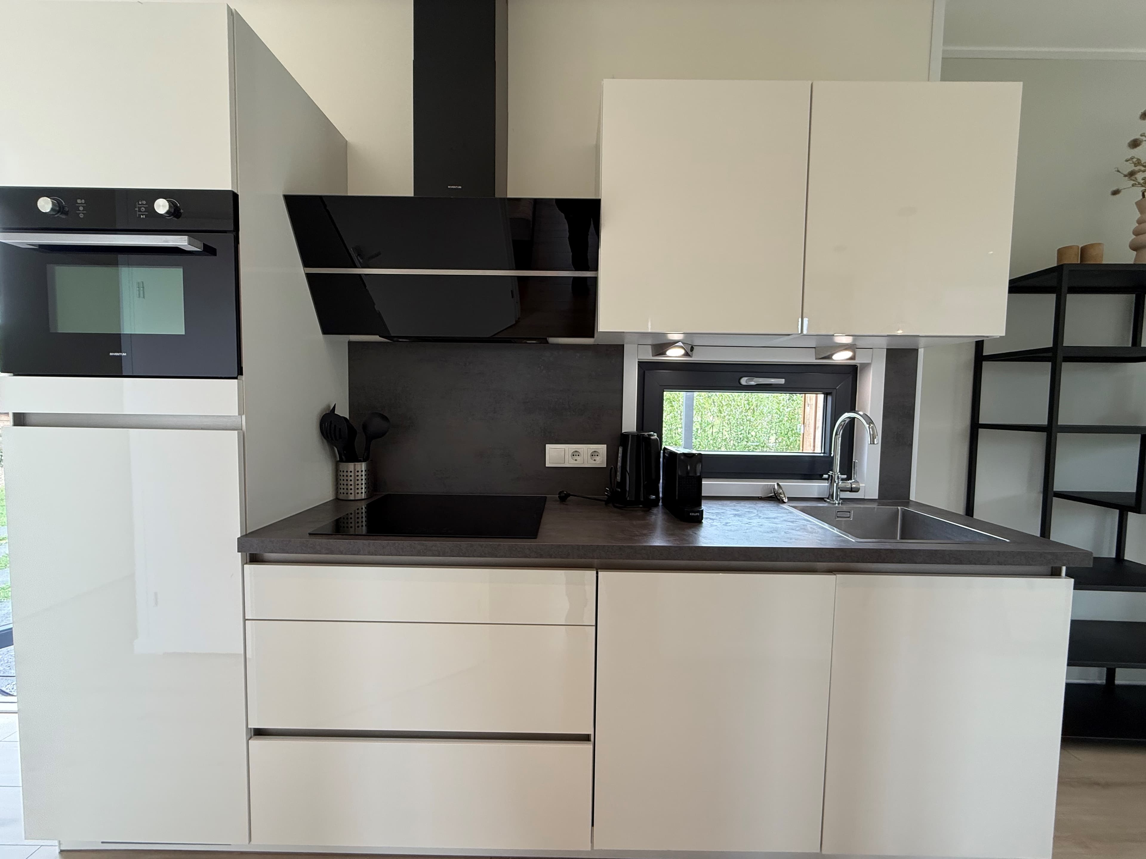 Moderne keuken met witte kastjes, inbouwapparatuur en een zwarte spoelbak in een recreatiewoning