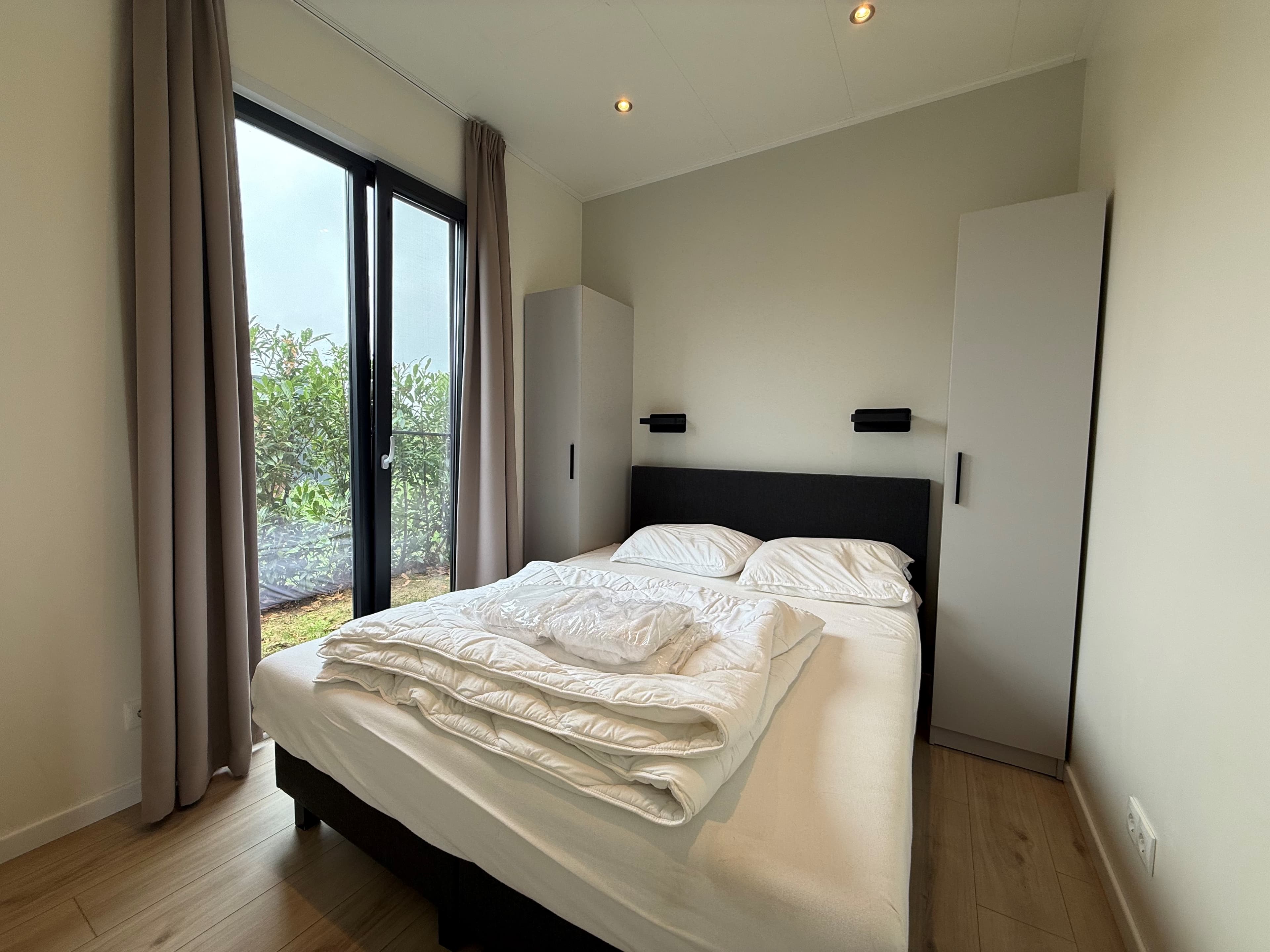 Slaapkamer met een tweepersoonsbed, kast en grote ramen met uitzicht op de buitenruimte.
