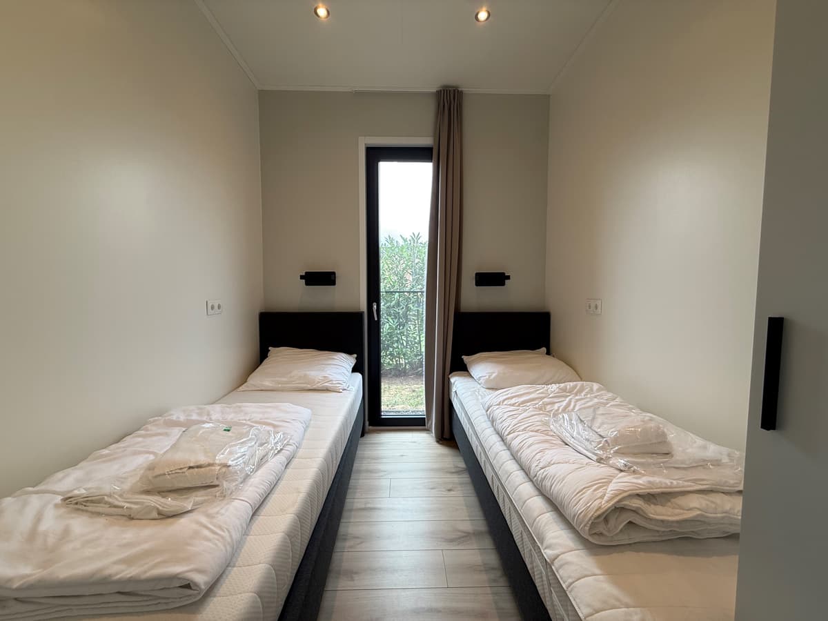 Slaapkamer met twee eenpersoonsbedden, ramen met uitzicht op de tuin en neutrale wandkleuren